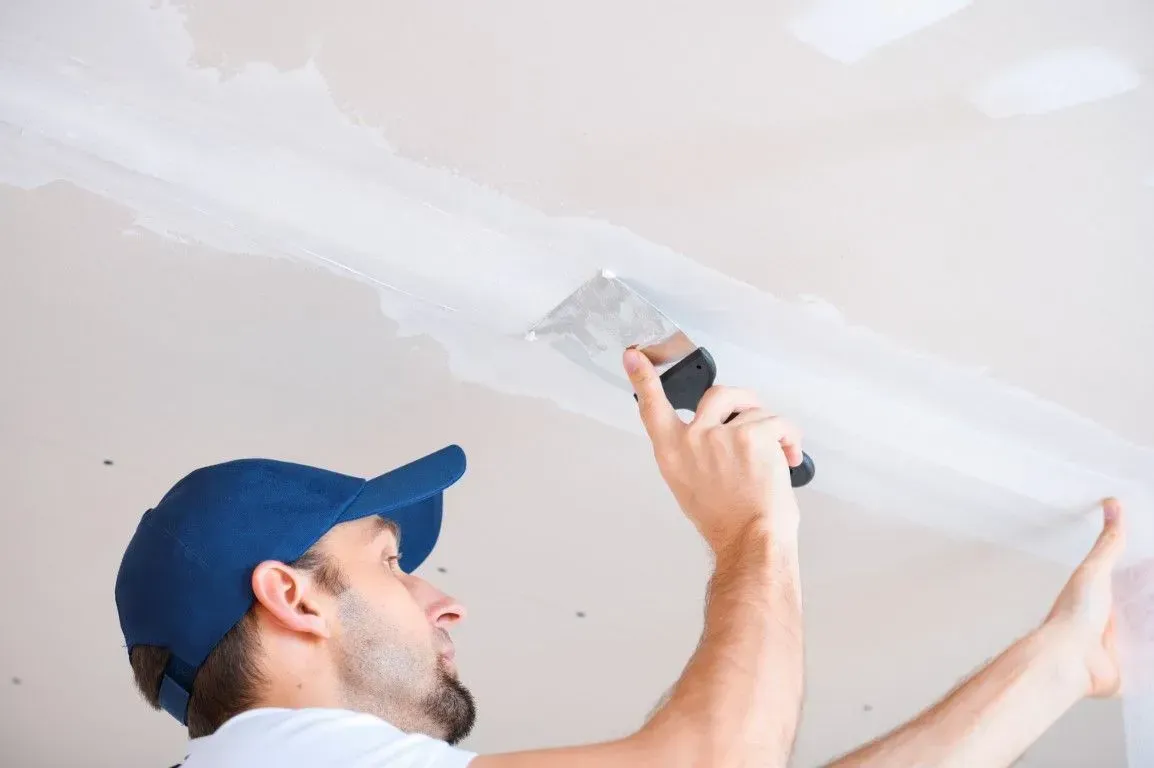 Man applying joint compound to a drywall ceiling seam.