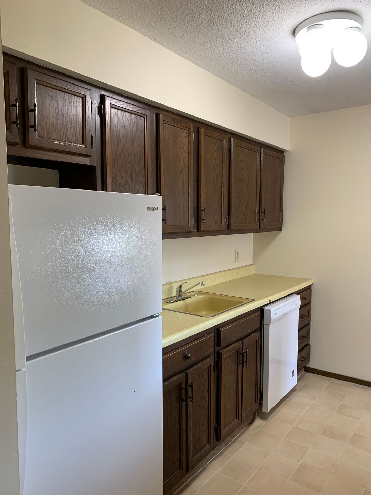 a kitchen with brown cabinets , a white refrigerator , a sink , and a dishwasher .