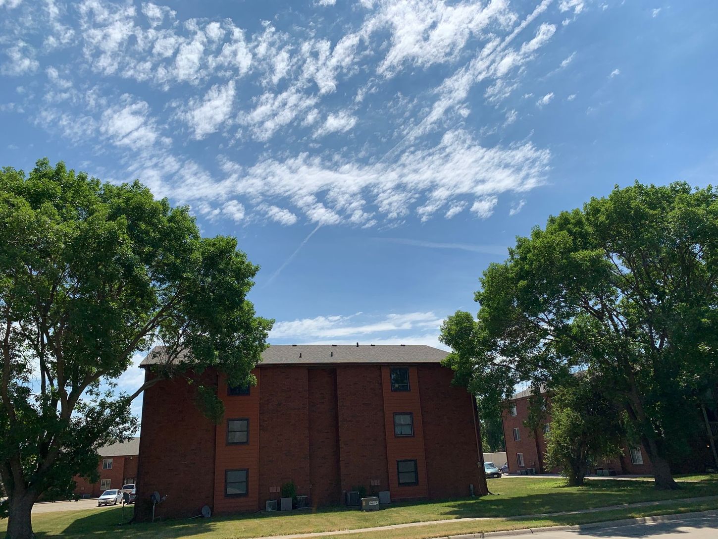 a brick building with trees in front of it and a blue sky with clouds