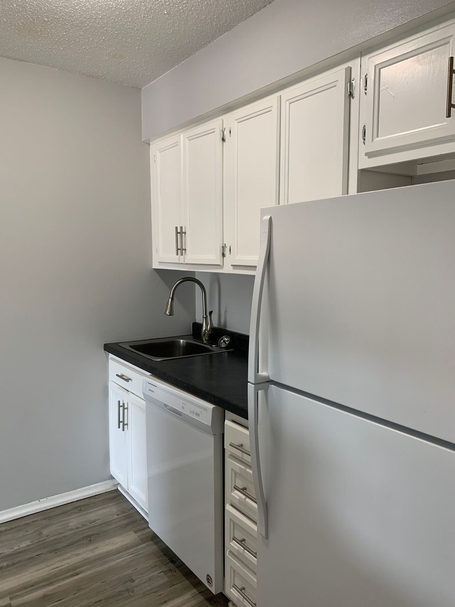 a kitchen with white cabinets , a refrigerator , a sink , and a dishwasher .