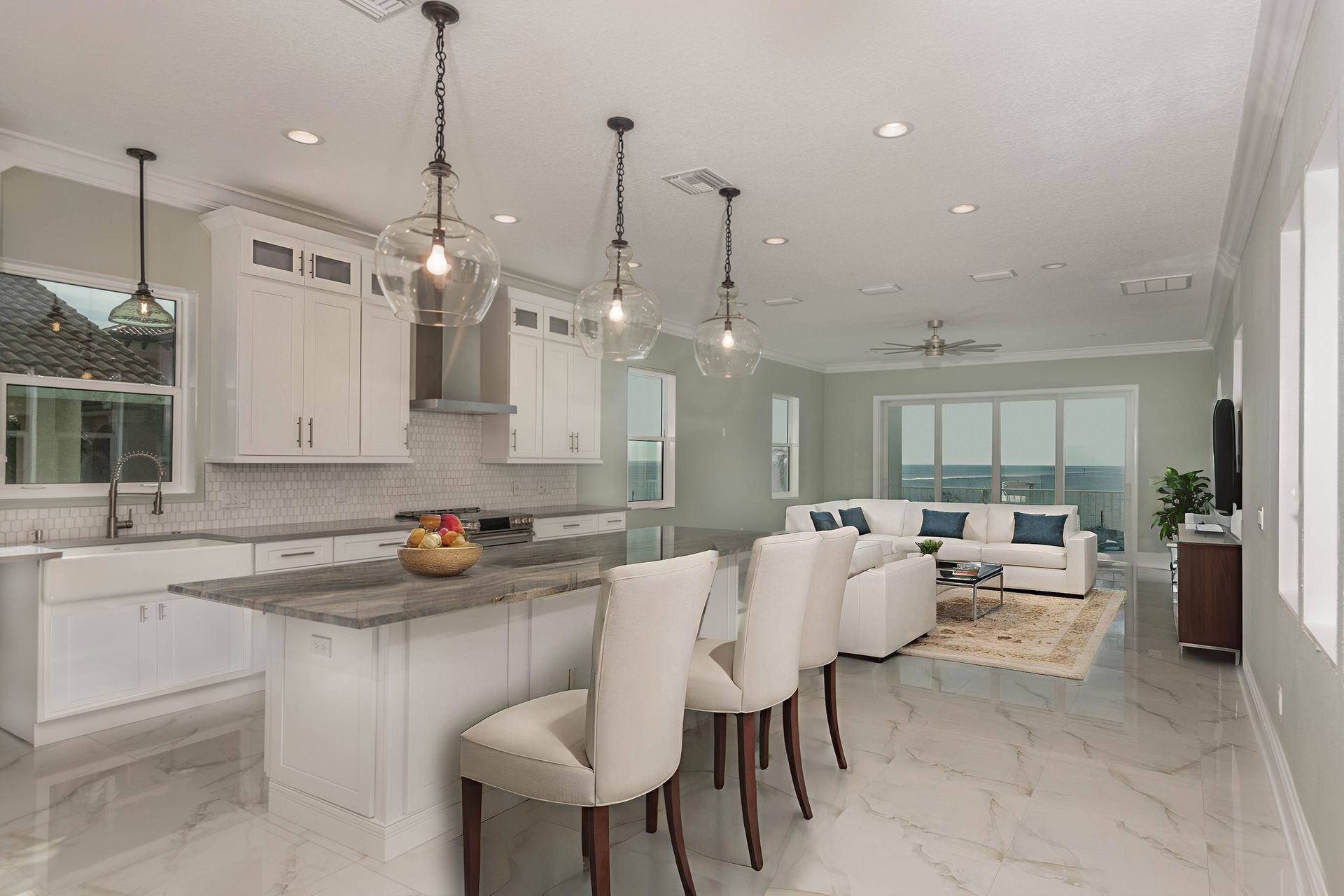 Open-concept kitchen and living area with white cabinets, marble countertops, pendant lights, and light tile flooring.