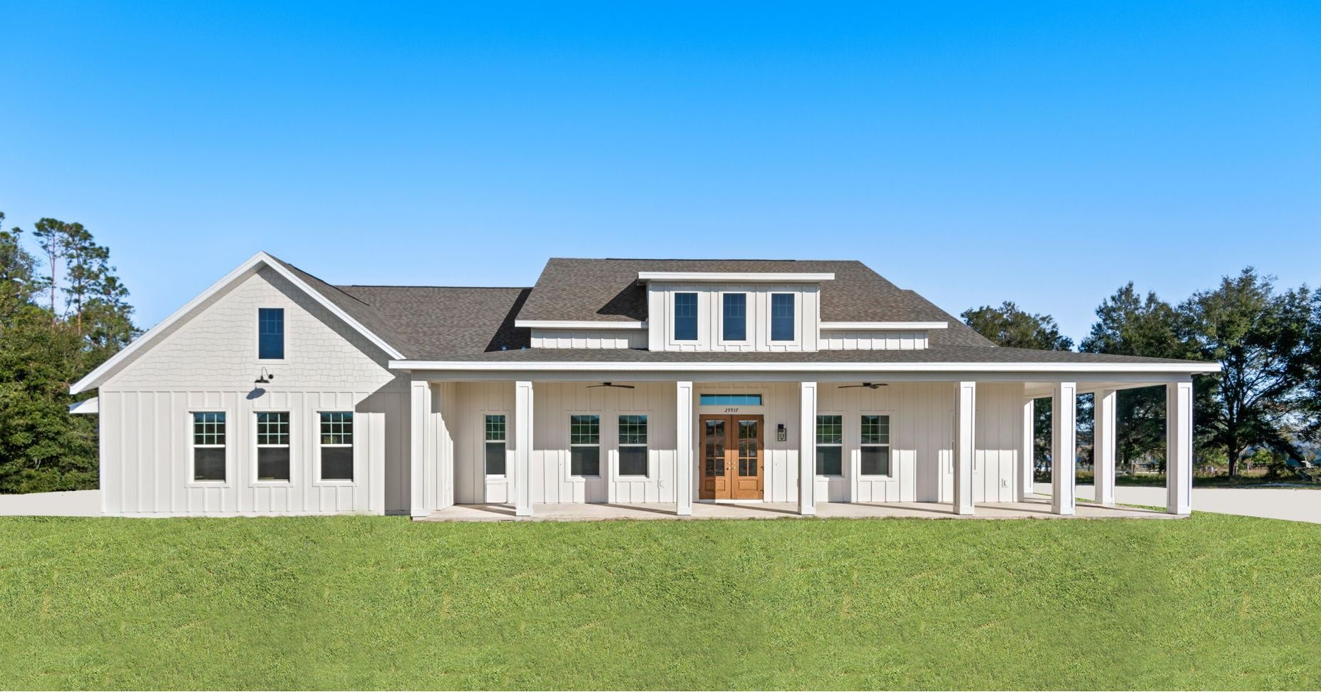 White farmhouse with a long porch, blue sky, and green grass.