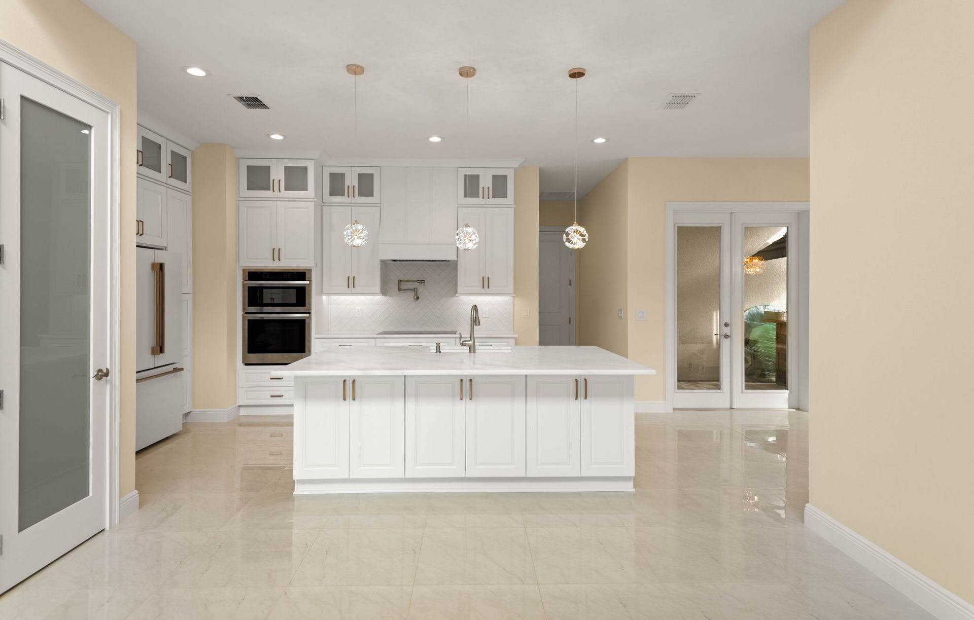 White kitchen with island, cabinets, appliances, and doors. Pale yellow walls and shiny, light-colored floor.