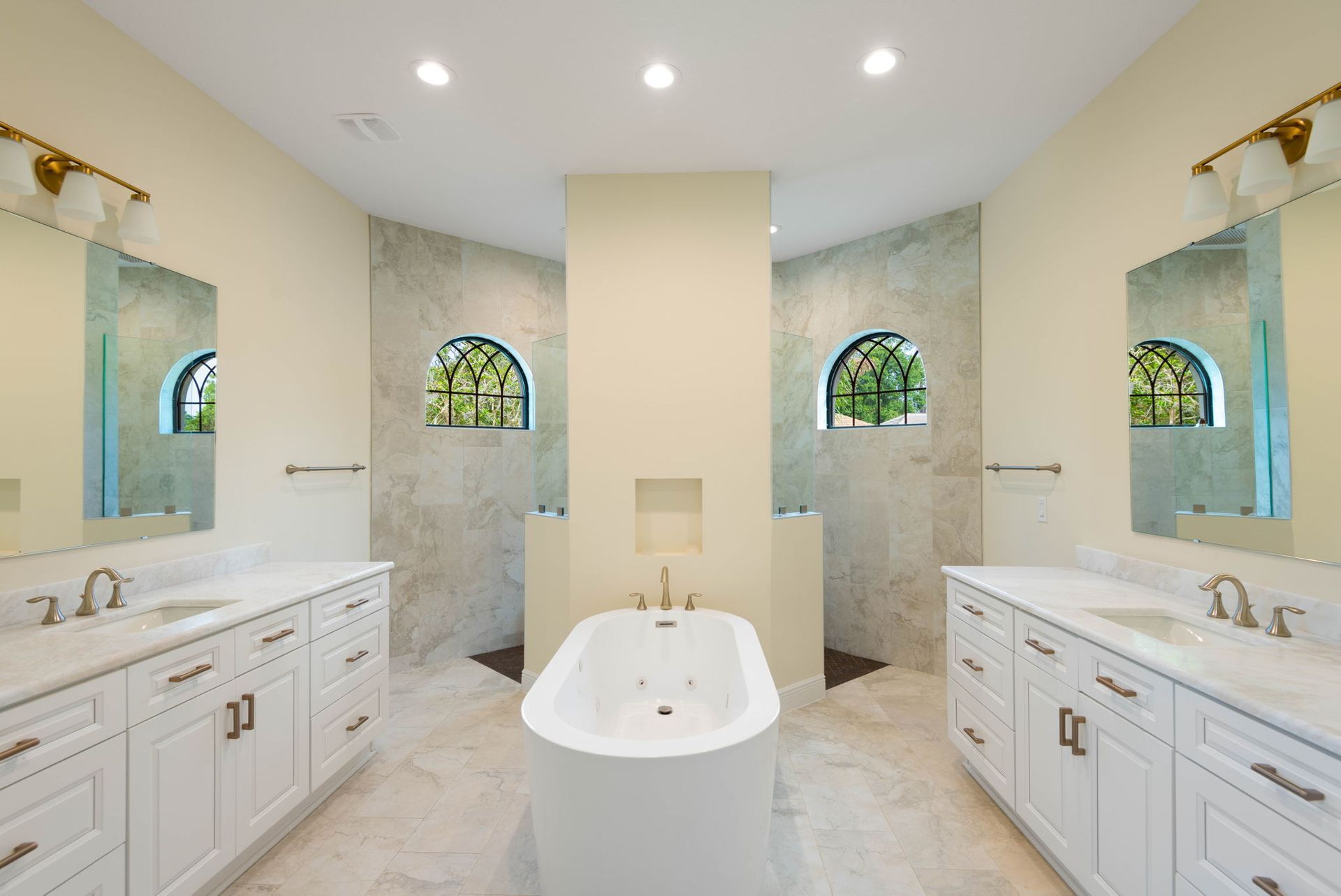 Spacious bathroom with white cabinetry, marble countertops, freestanding tub, and two showers.