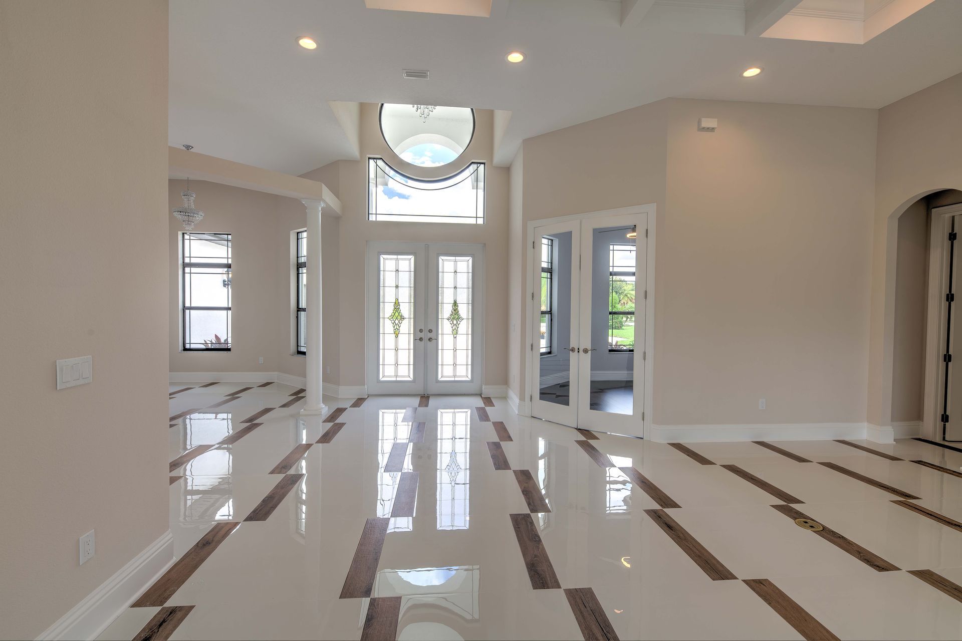 Spacious entryway with glossy tiled floor, double doors, arched window, and neutral walls.