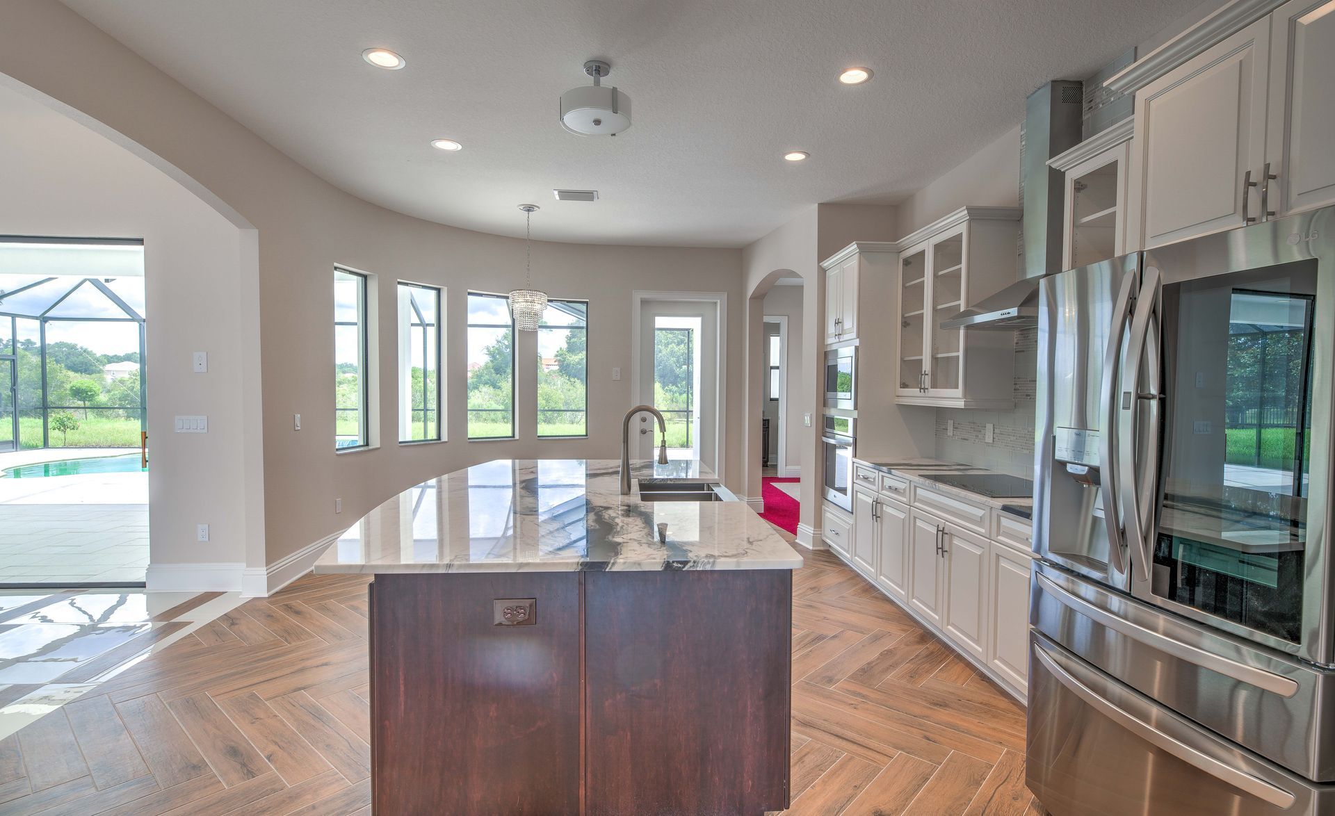 Modern kitchen with curved island, stainless steel appliances, and large windows.