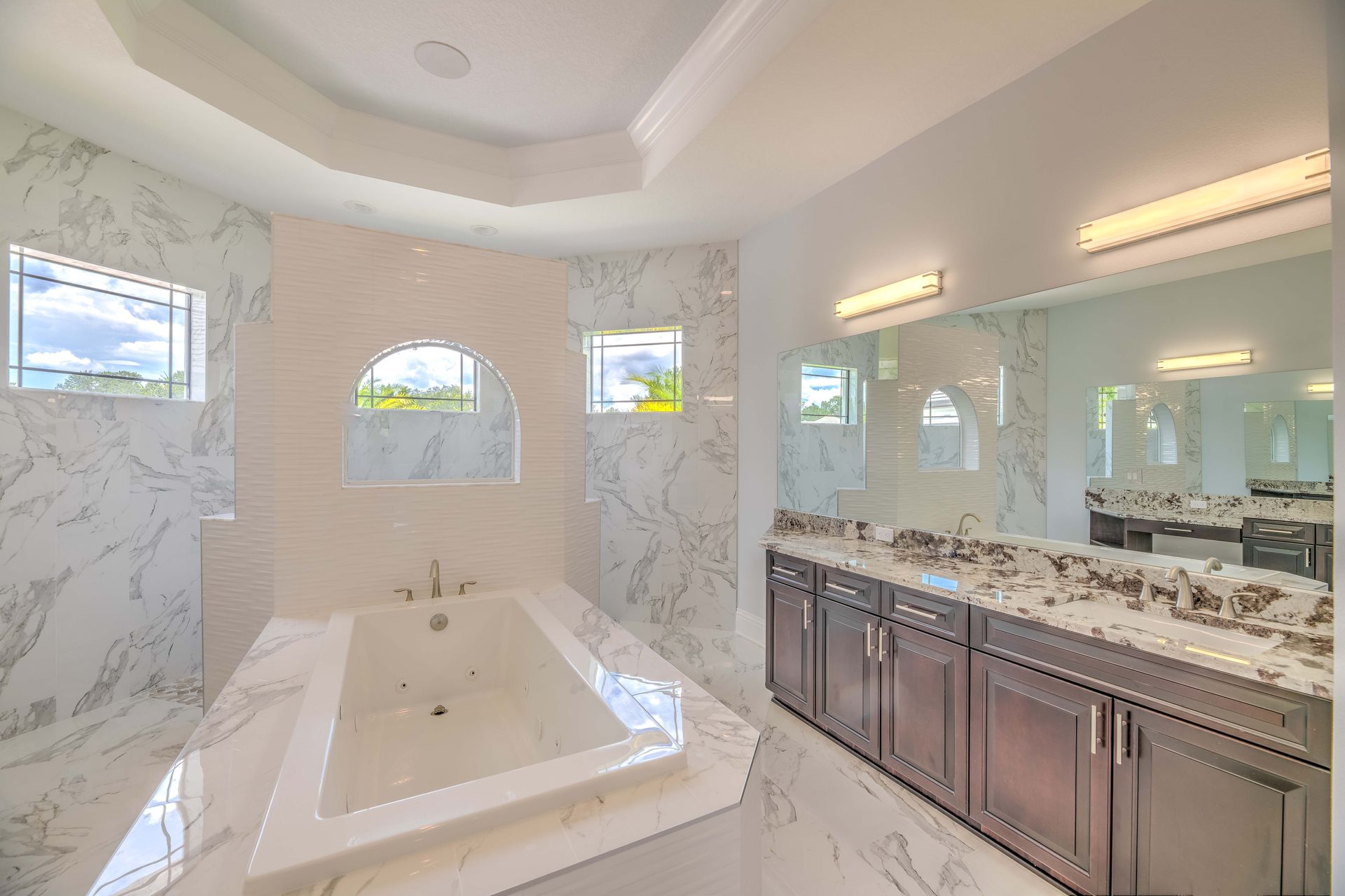 Luxurious bathroom with marble walls, soaking tub, vanity, and large mirror.