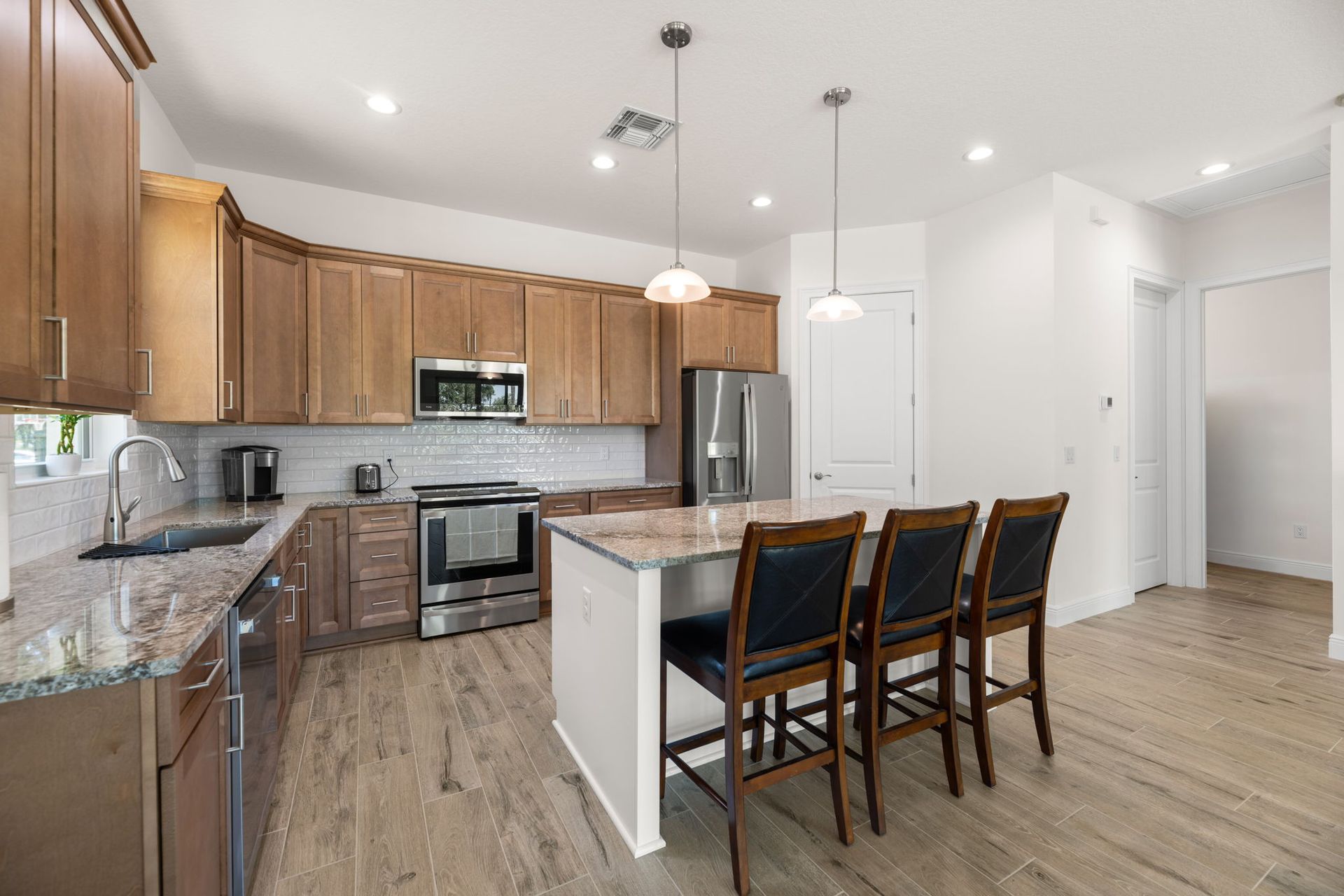 Kitchen with wood cabinets, island with stools, stainless steel appliances, and light wood flooring.
