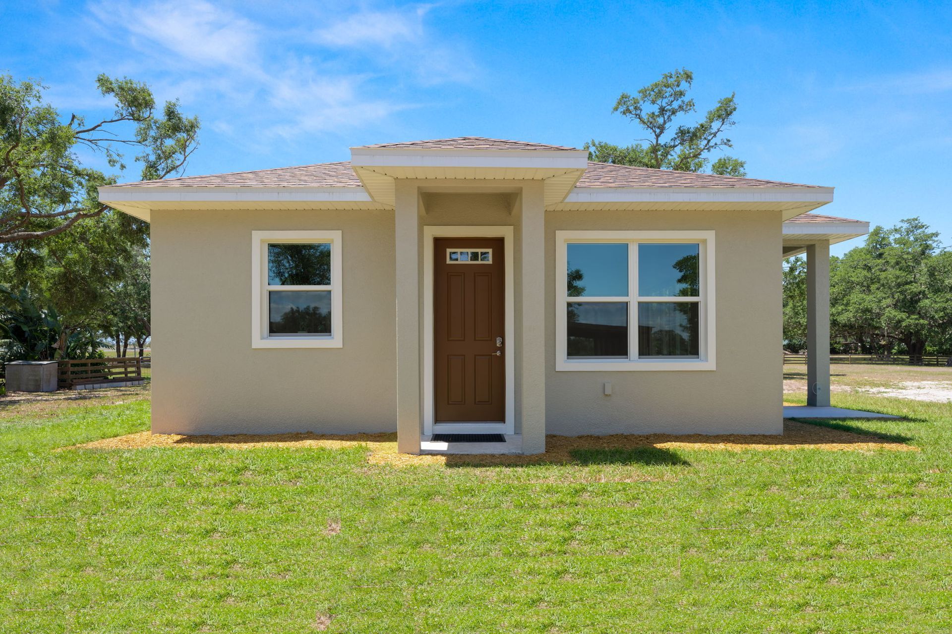 Small beige house with brown door, white window frames, and green lawn under a blue sky.