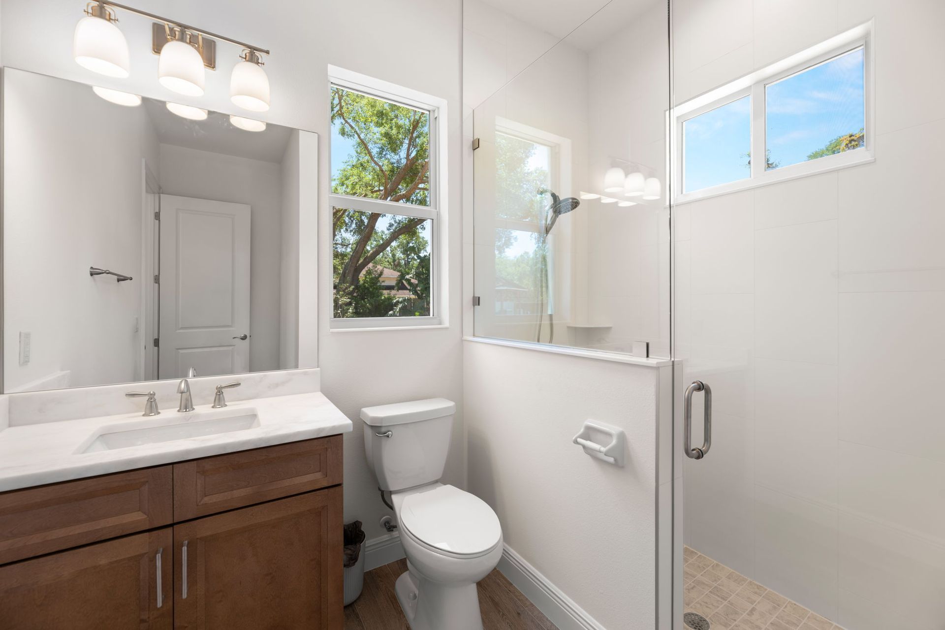 Bathroom with vanity, toilet, and shower with glass door. Window with a tree view.