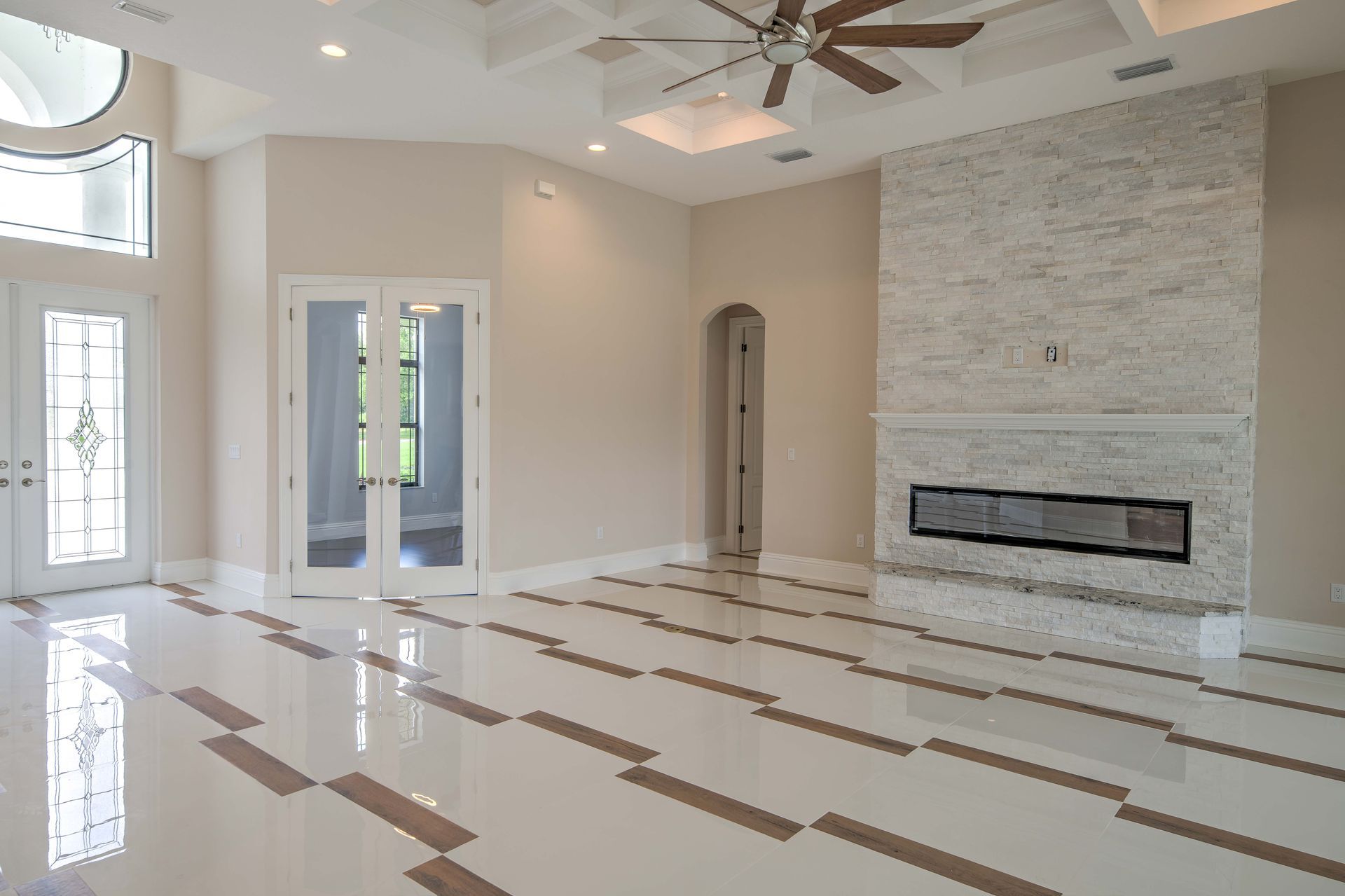 Spacious room with white and tan tile floor, fireplace, French doors, and ceiling fan.
