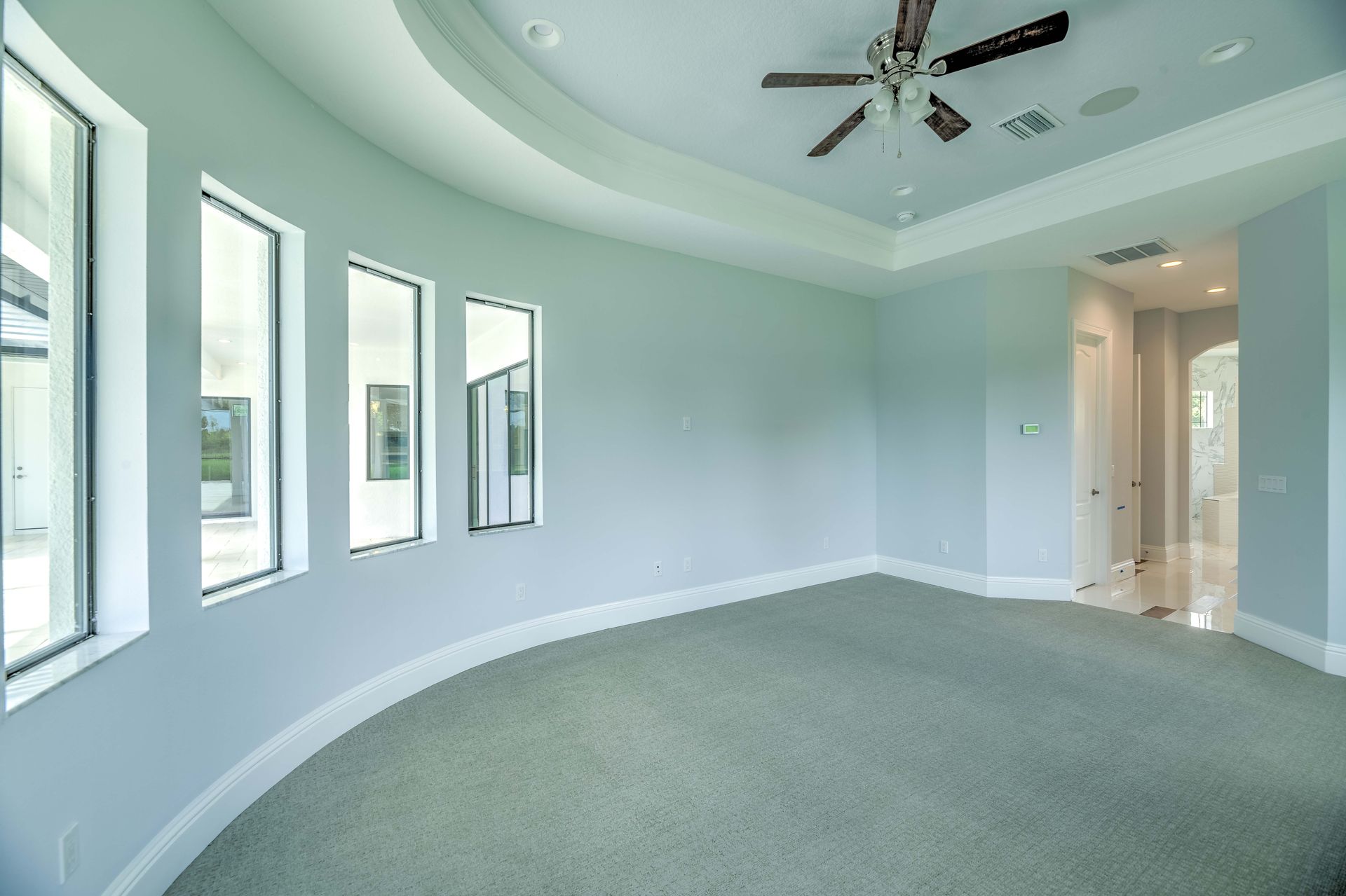 Empty bedroom with curved walls, three tall windows, and a carpeted floor.