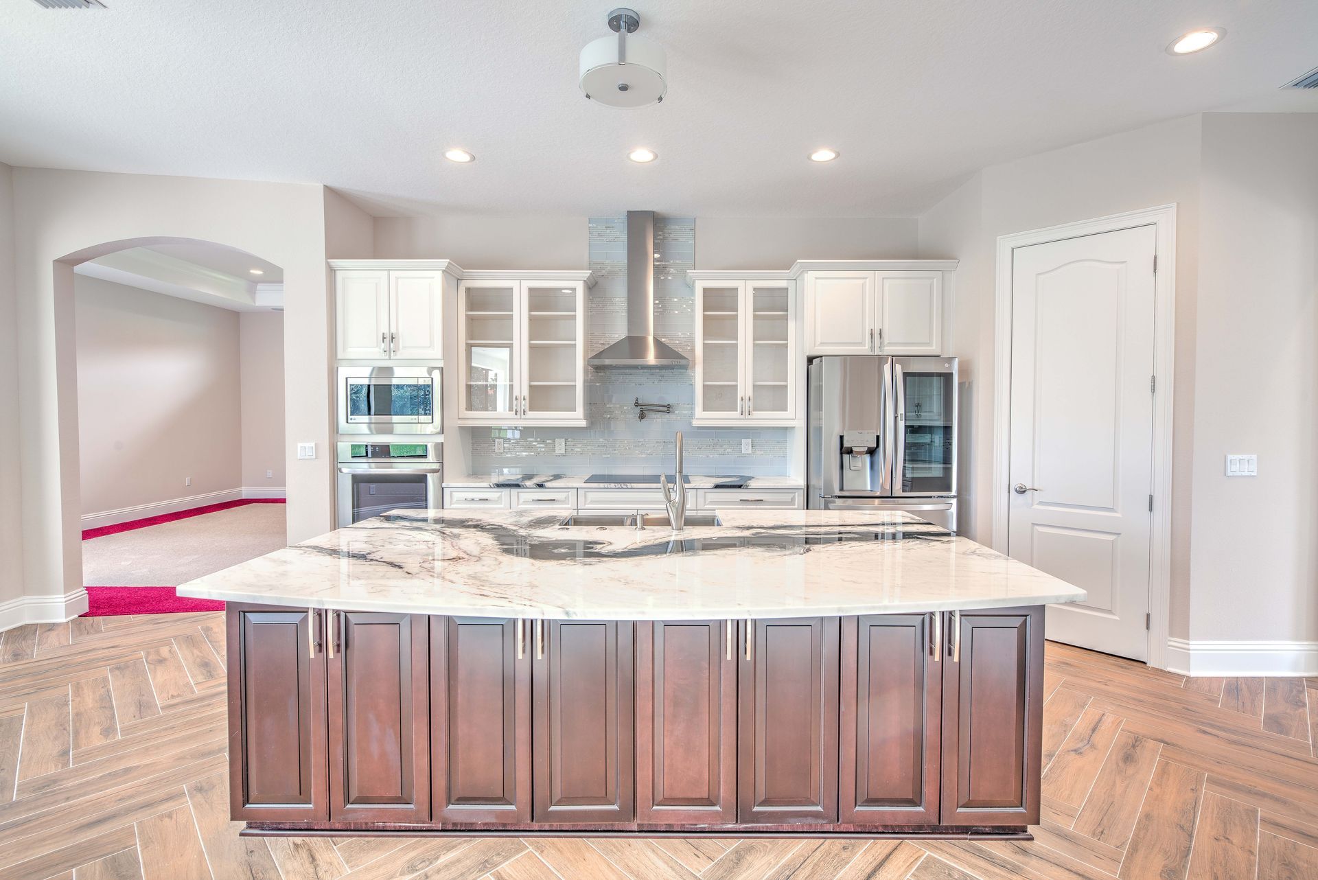 Kitchen with dark island and light countertops, white cabinets, stainless steel appliances, and herringbone floors.
