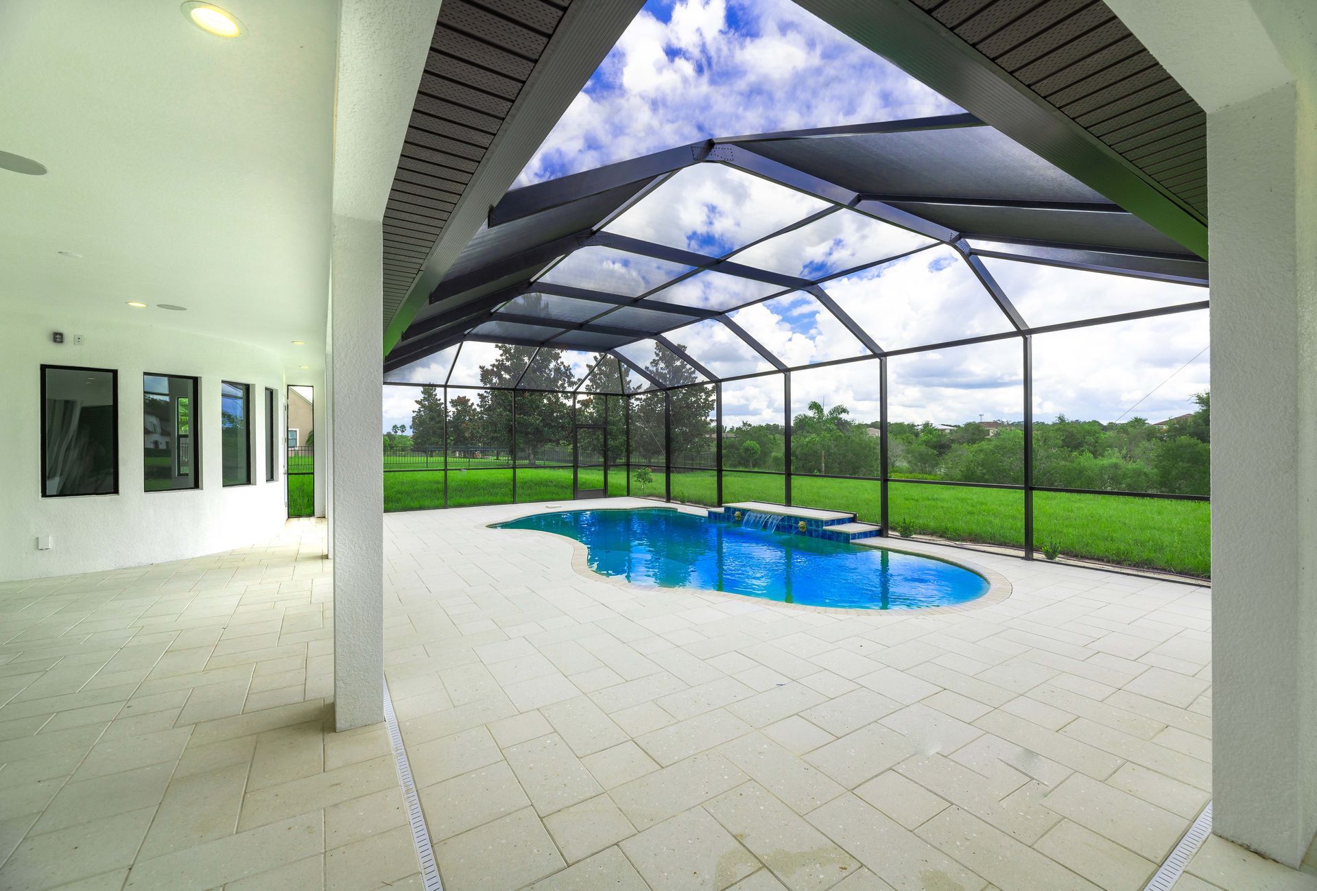 Pool under a screened enclosure with blue water, surrounded by tile and a lawn.