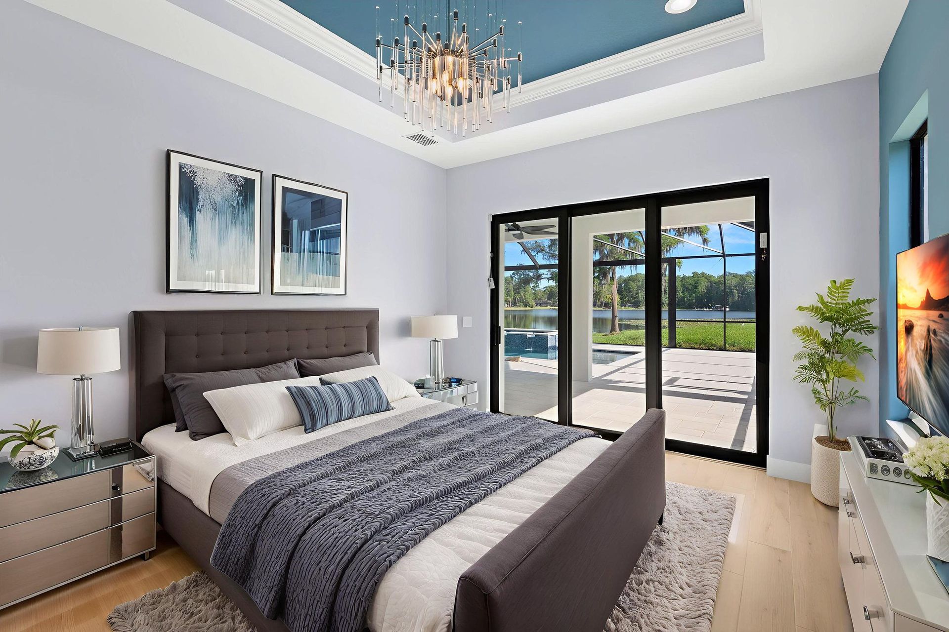 Bedroom with bed, art, and doors to a patio overlooking a pool and yard, light blue walls and ceiling.