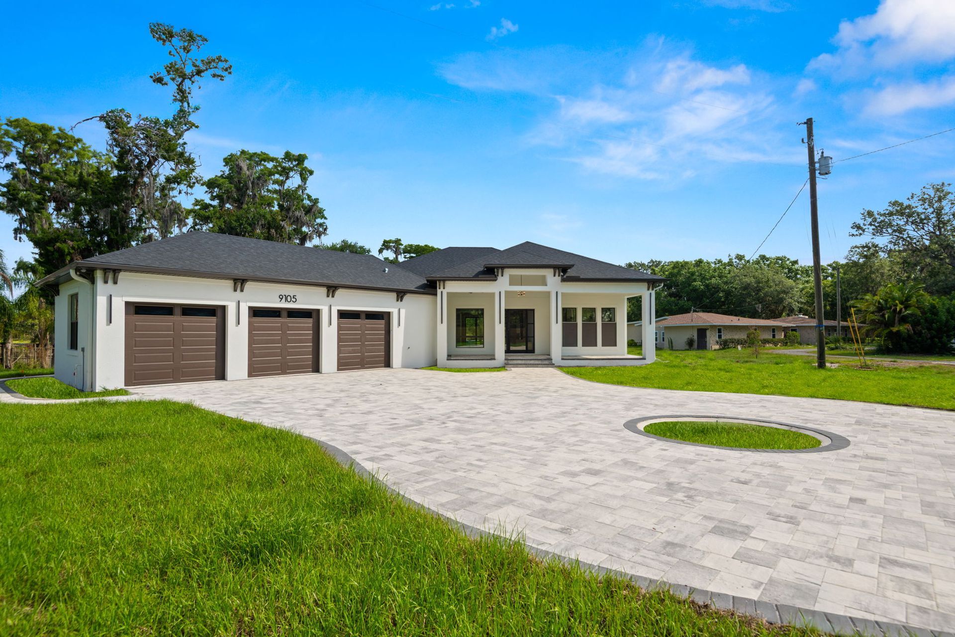 White house with a three-car garage and gray paver driveway under a blue sky.