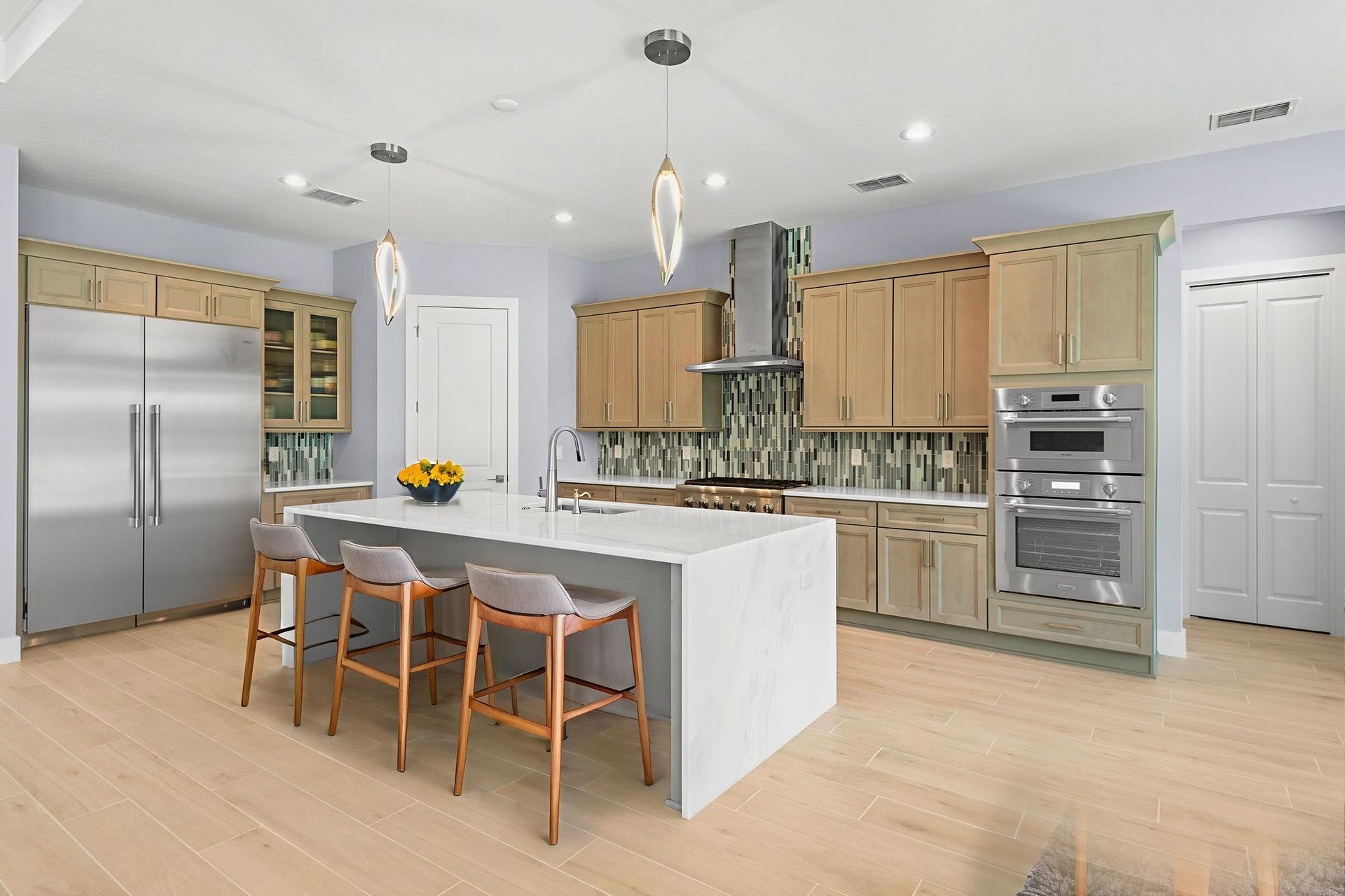 Modern kitchen with light wood cabinets, stainless steel appliances, and a large island with bar stools.