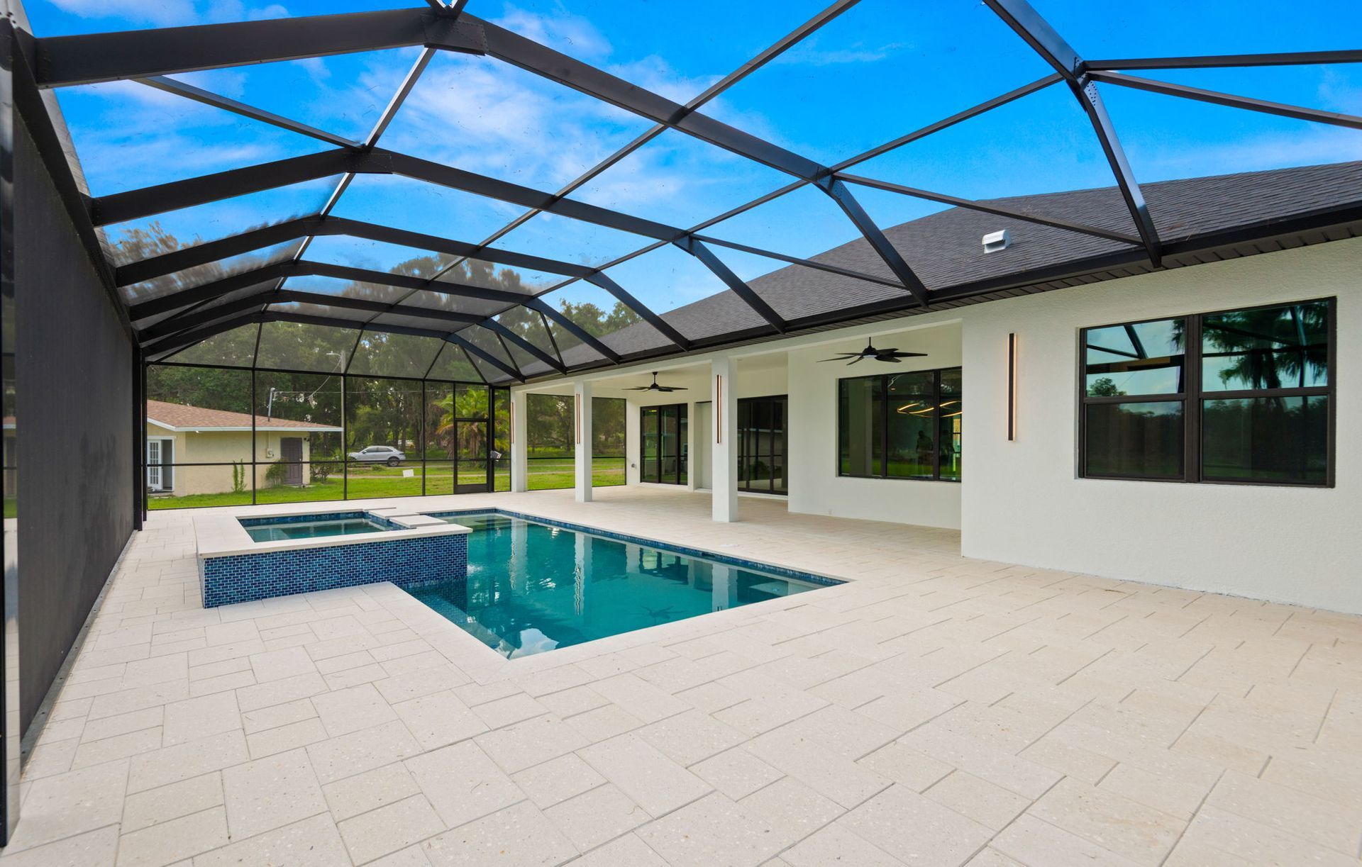 Pool enclosure with pool and spa, white patio, and a sunny sky.