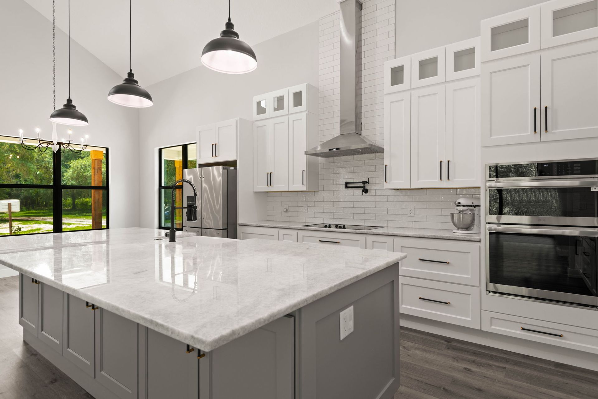 Modern kitchen with gray island, white cabinets, stainless steel appliances, and pendant lights.