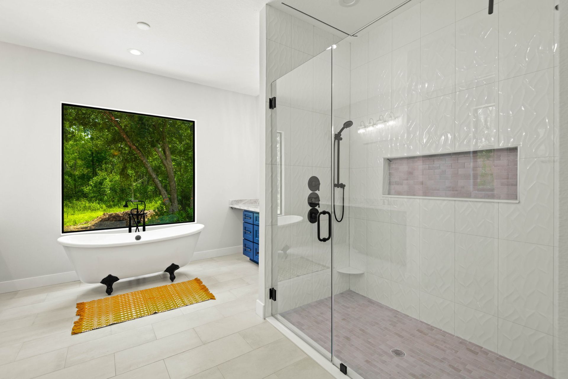 Modern bathroom with a glass shower, soaking tub by a window, and blue cabinet.