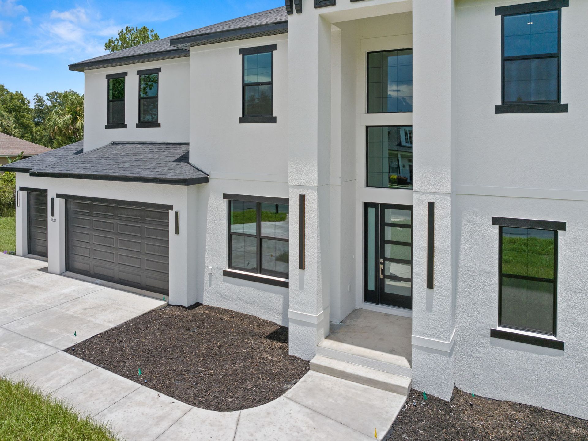 Modern white two-story house with black trim, dark garage door, and entry door, on a sunny day.