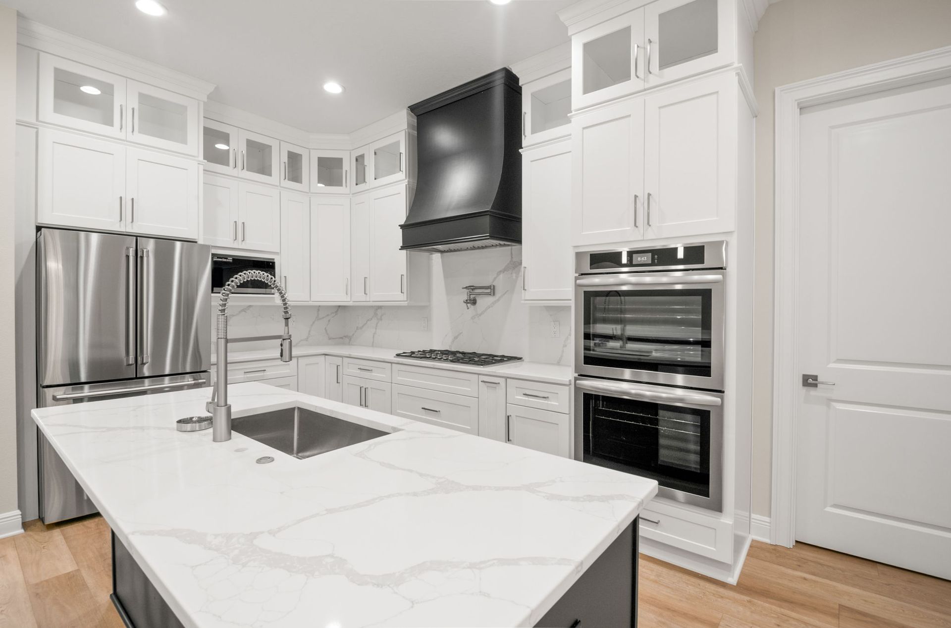 Bright white kitchen with stainless steel appliances, black range hood, and white countertops.