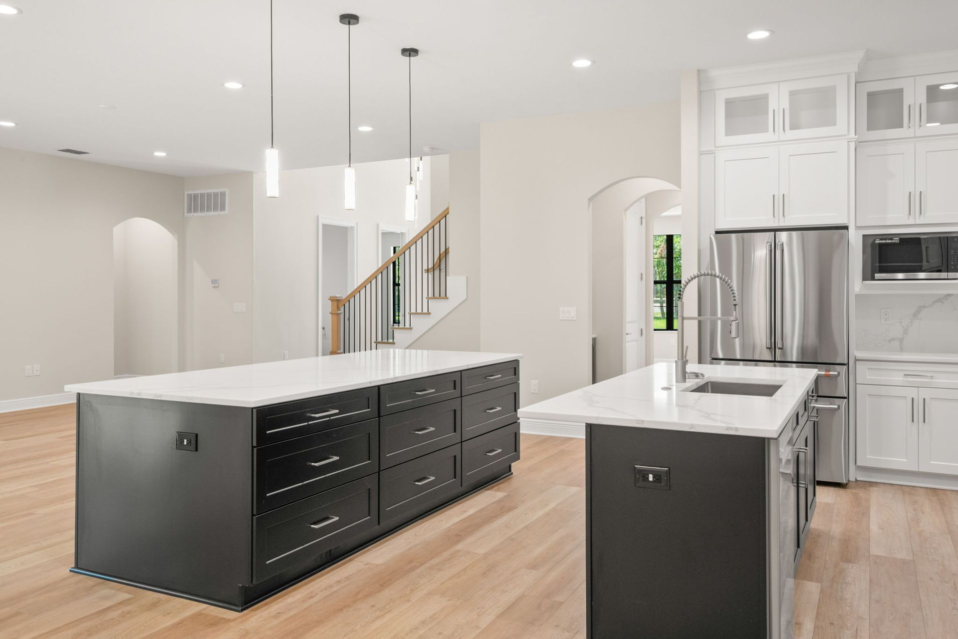 Modern kitchen with two dark islands, white countertops, and stainless steel appliances.