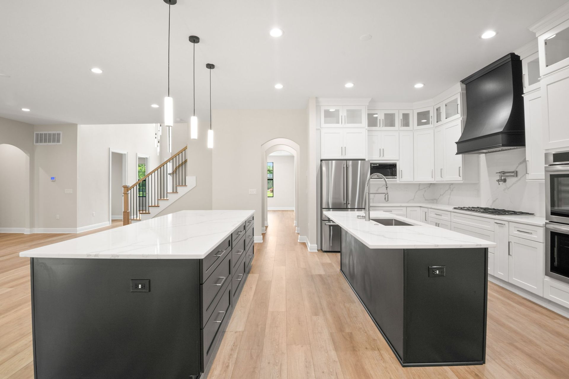 Modern kitchen with white countertops, dark gray cabinets, two islands, and stainless steel appliances.