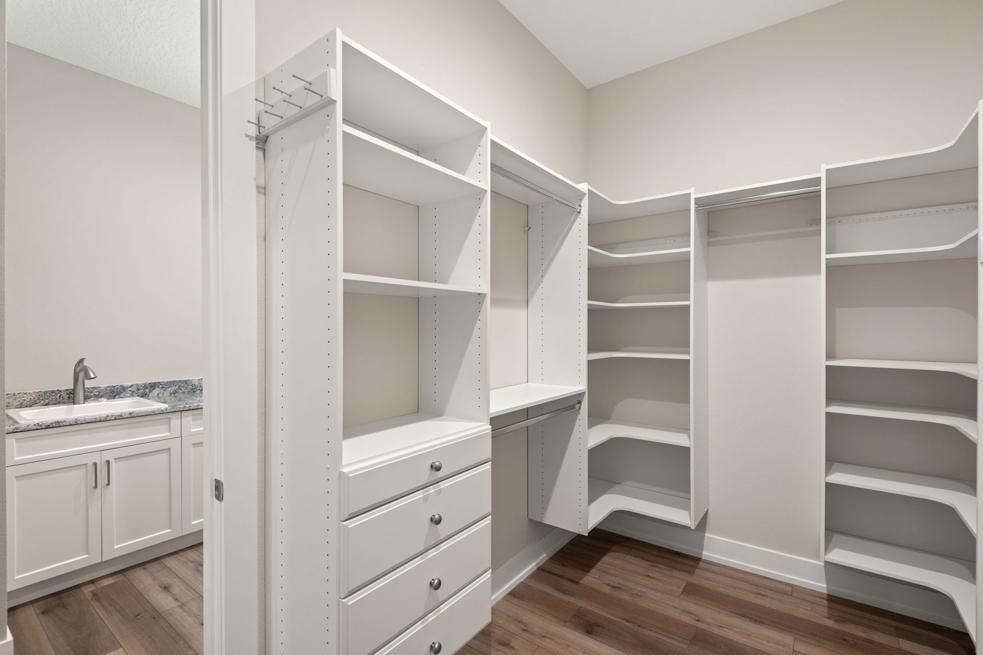 Walk-in closet with white shelving and drawers, a sink and cabinet area, and wood-look flooring.