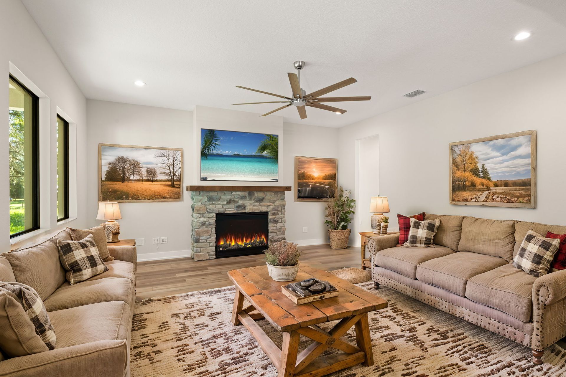 Living room with fireplace, sofas, artwork, and ceiling fan. Warm colors, cozy setting.