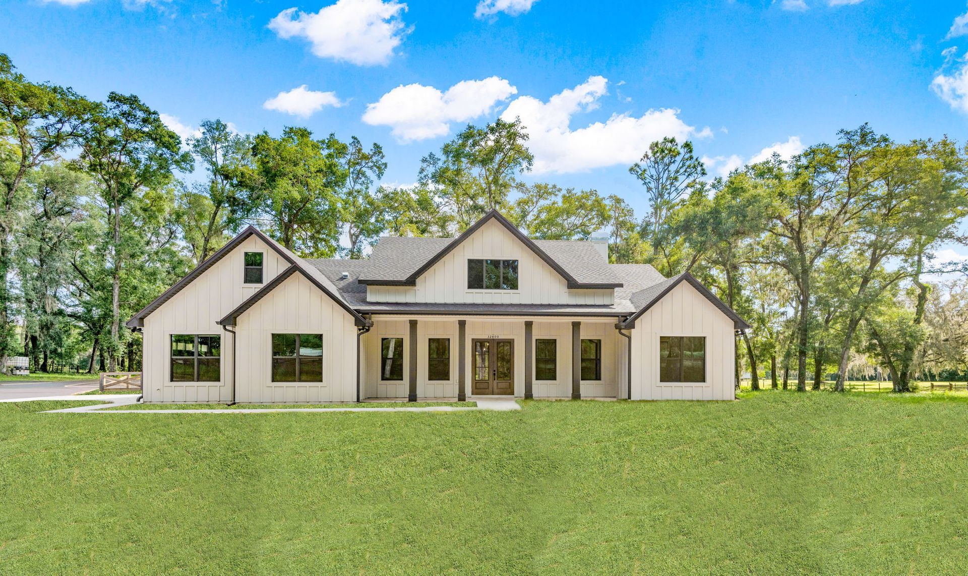 White farmhouse with dark trim, gray roof, and large front yard, under a blue sky.