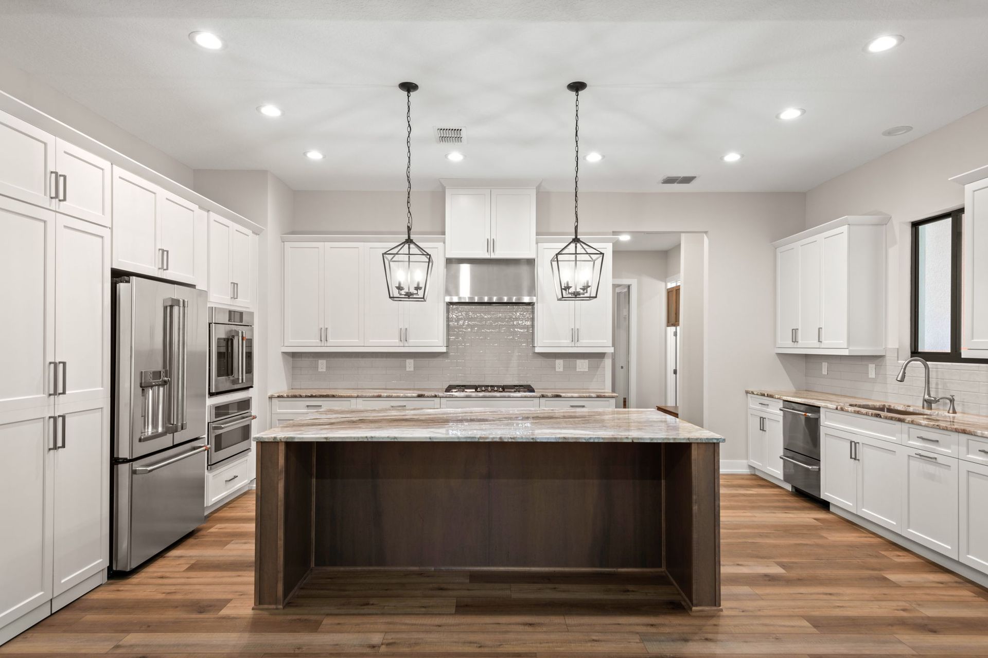 Modern white kitchen with island, stainless steel appliances, and wood flooring.