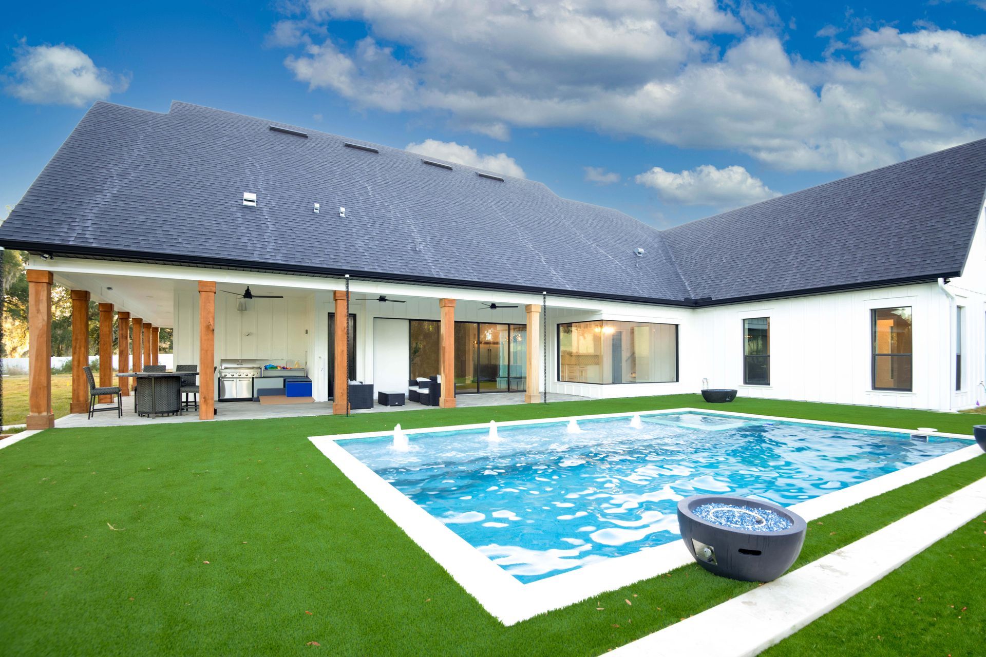 Backyard with pool, white house, dark roof, artificial green grass, and outdoor fireplace.