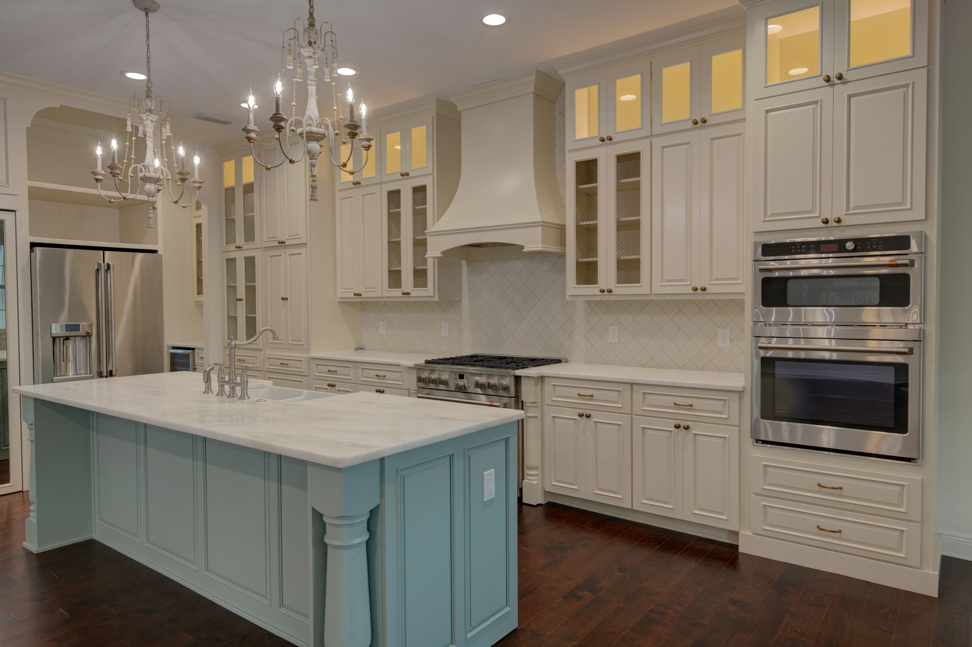 Elegant kitchen with blue island, white cabinets, stainless steel appliances, and chandeliers.