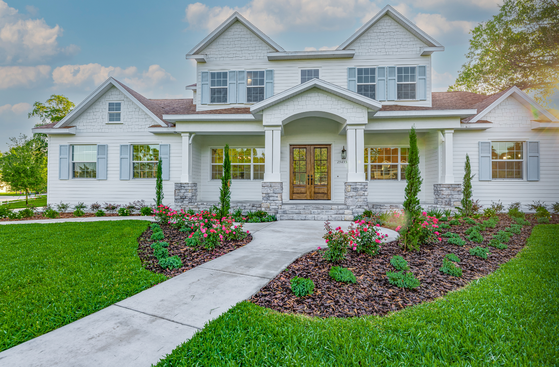White two-story house with light blue shutters, a brown door, and a landscaped walkway.