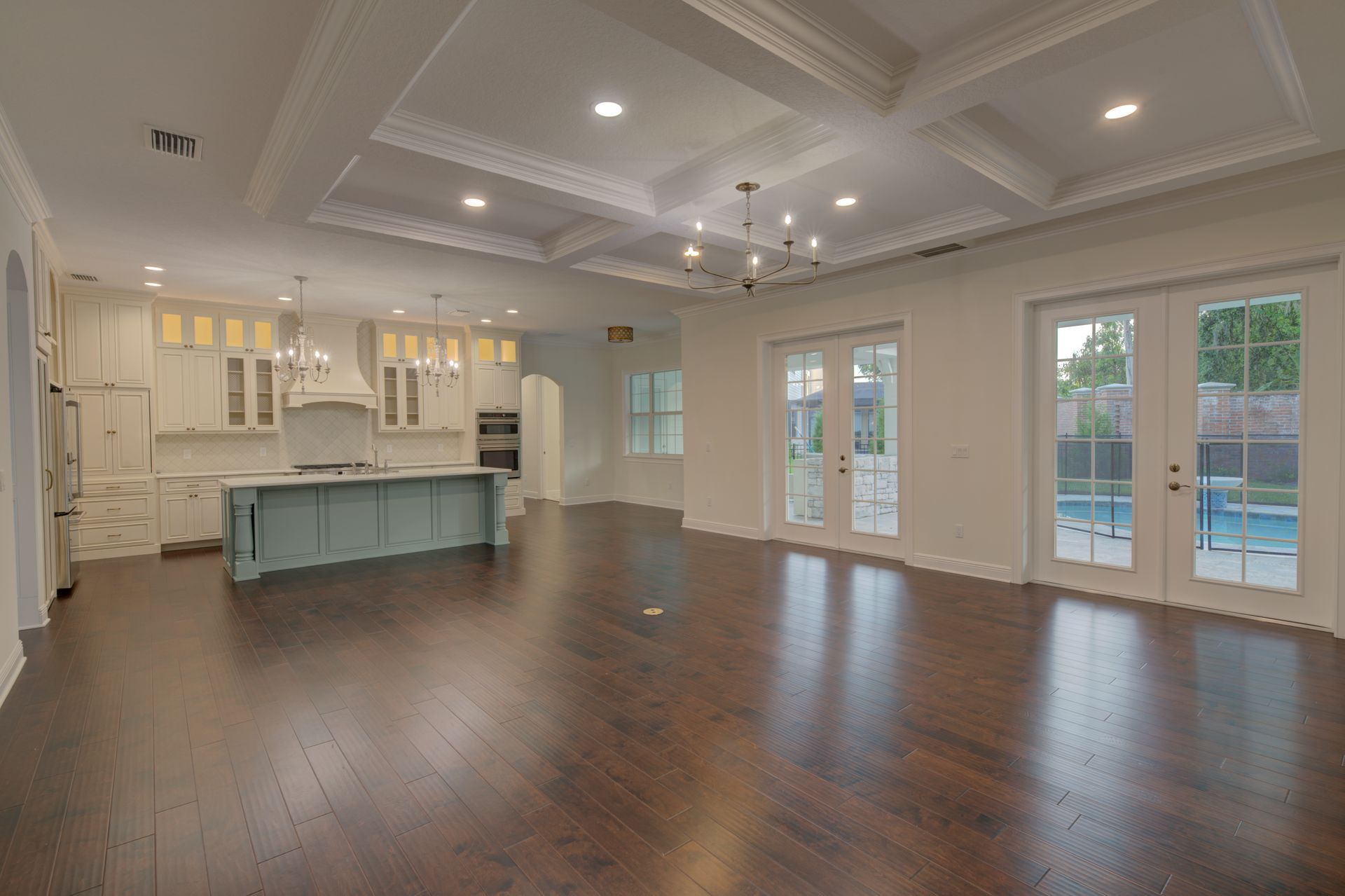 Spacious, open-concept living area with dark wood floors, a kitchen with blue island, and a pool outside the french doors.