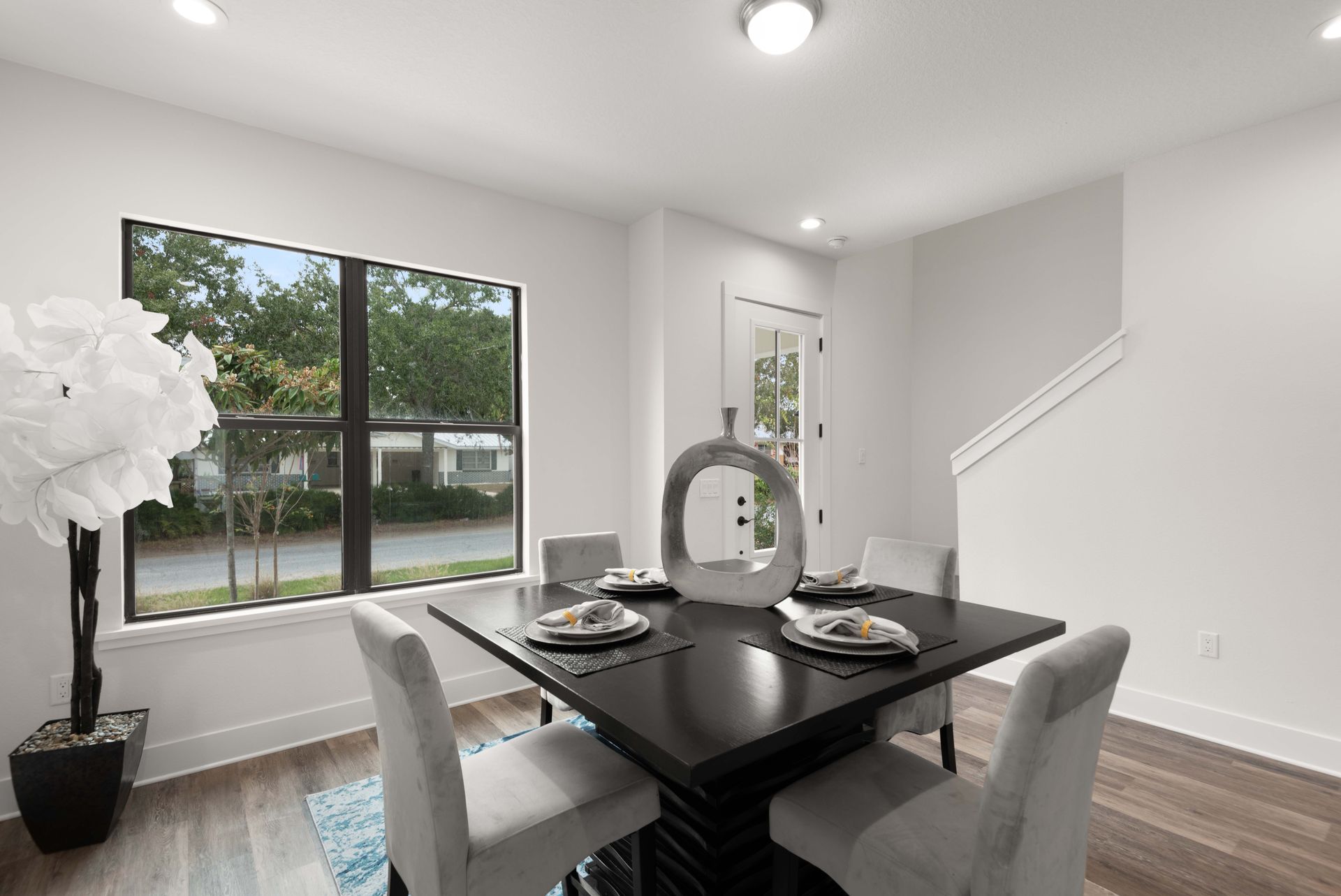 Dining room with dark square table, four white chairs, window, and decorative plant.