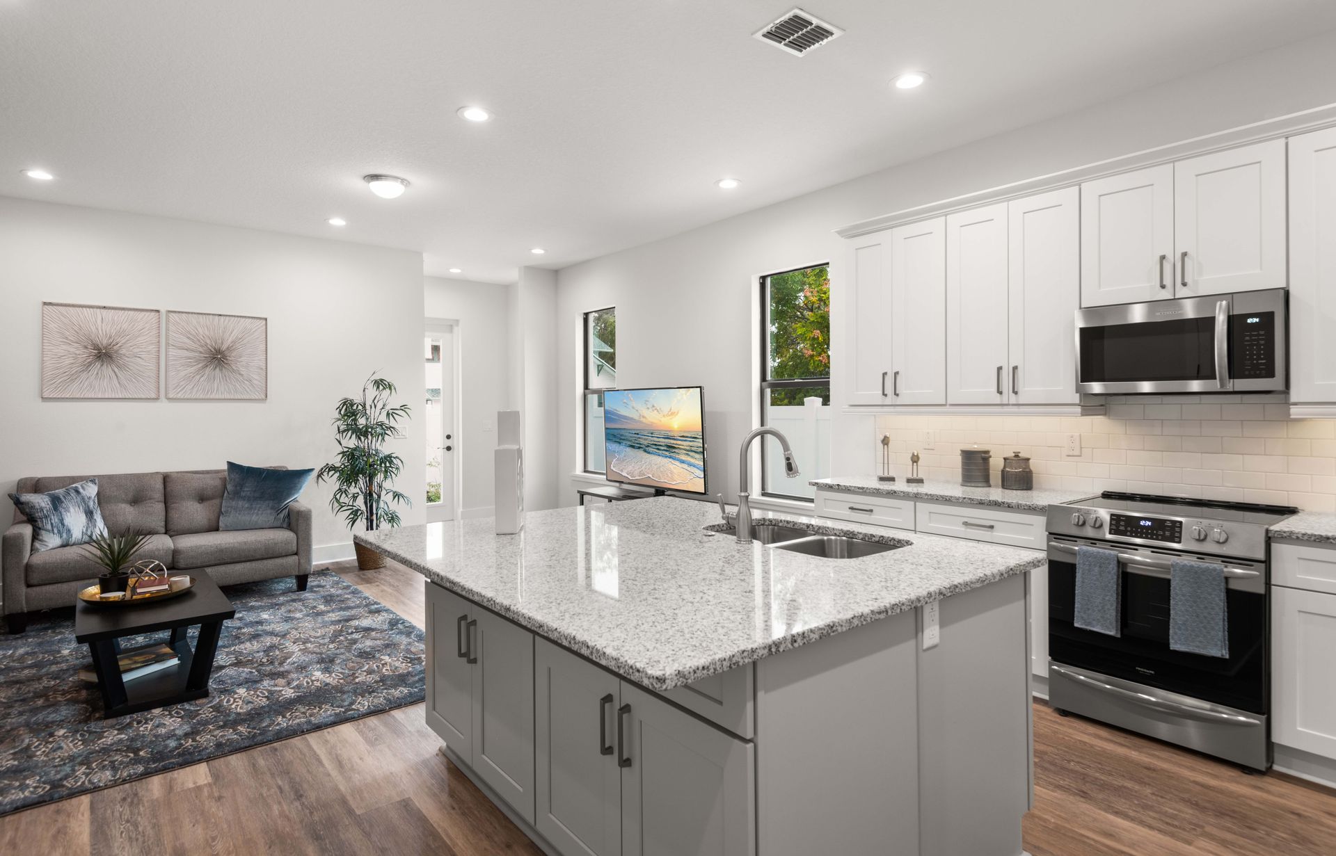 Open-concept kitchen and living area with gray cabinets, stainless steel appliances, and a granite countertop island.
