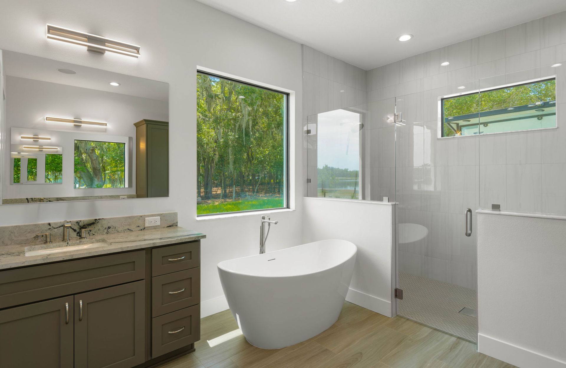 Modern bathroom with a white tub, large window, shower, and vanity.