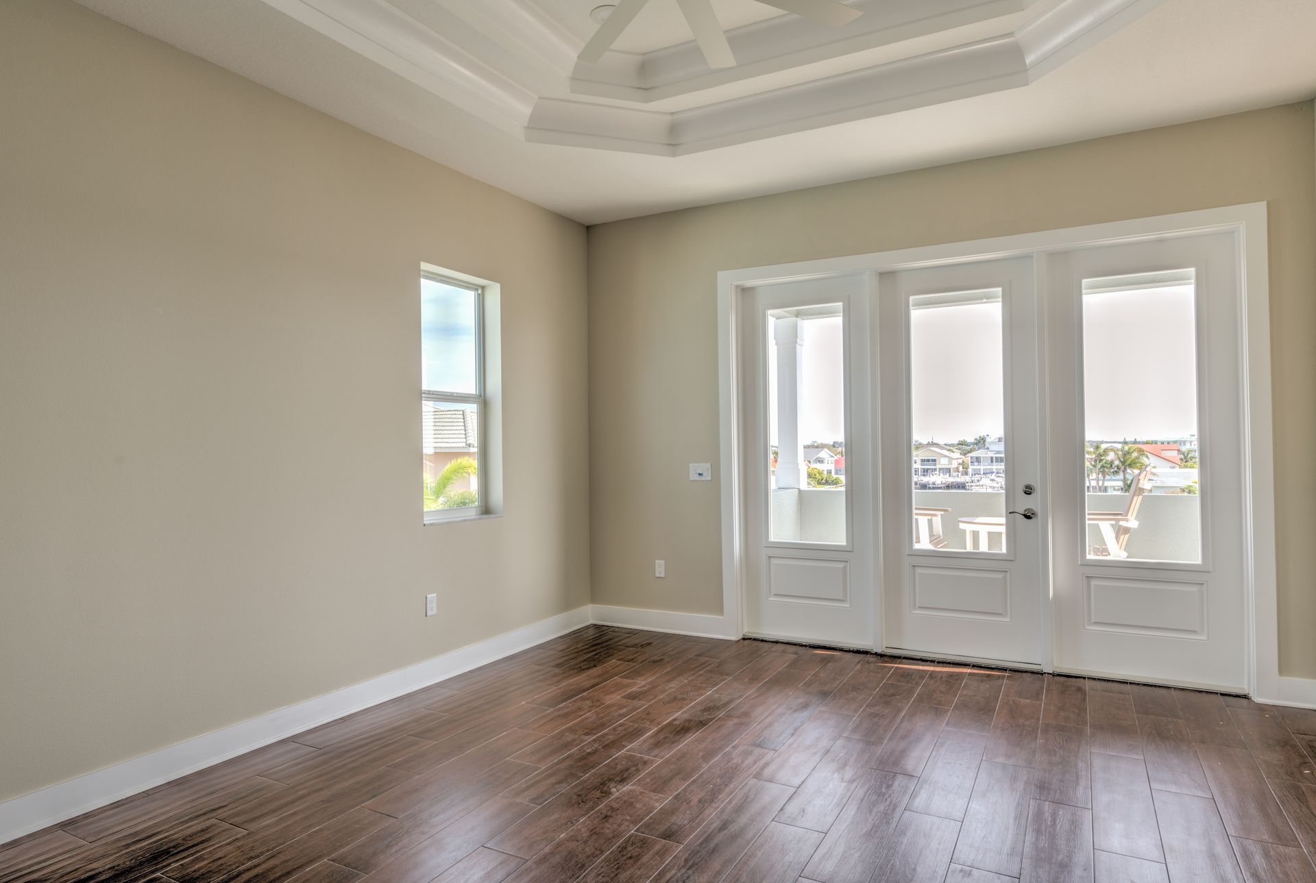 Empty room with dark wood floor, tan walls, and white French doors. A small window is on the left.