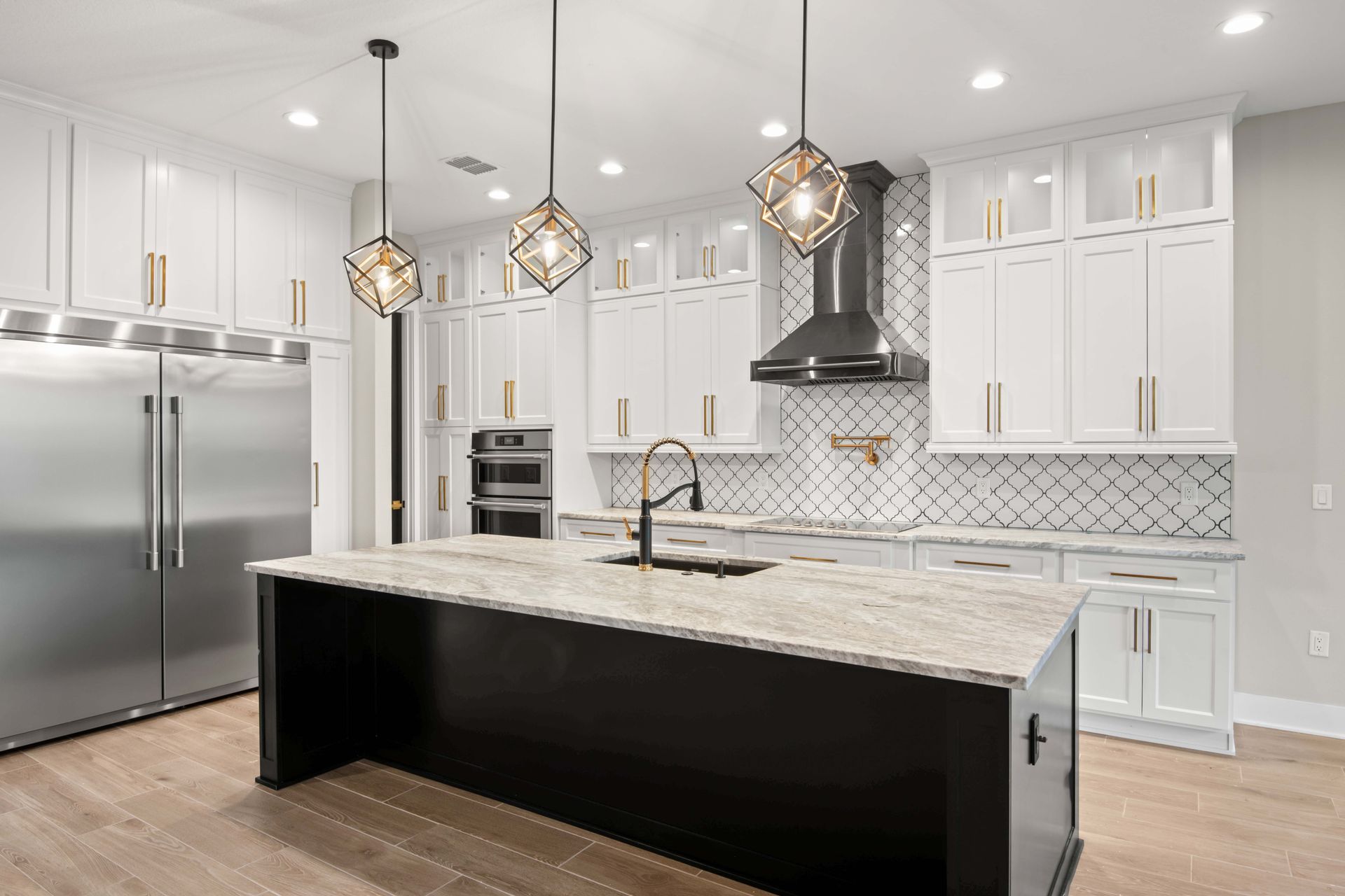Modern white kitchen with black island, stainless steel appliances, and pendant lights.