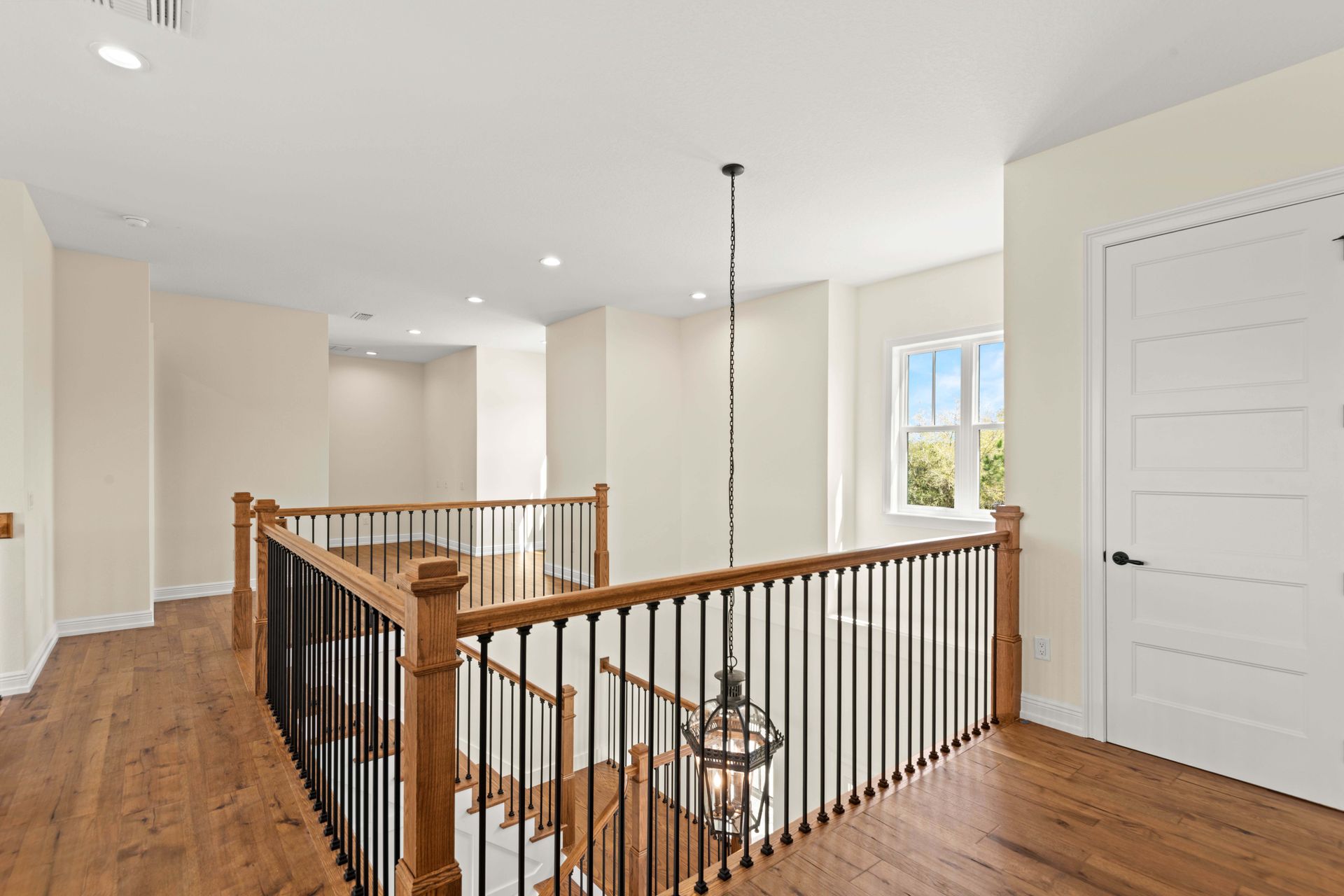Hallway with wood floors, black railing, and white walls, a pendant light hangs from the ceiling.