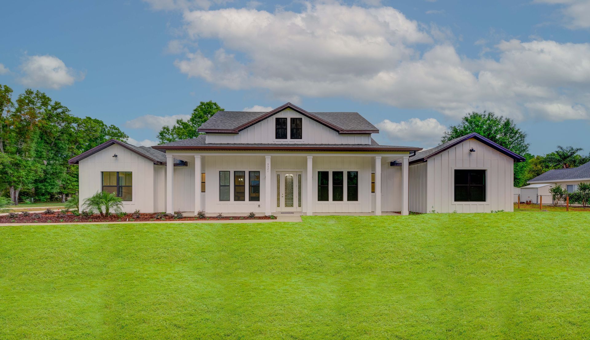 White farmhouse with black roof and windows against a blue sky with clouds, on a green lawn.