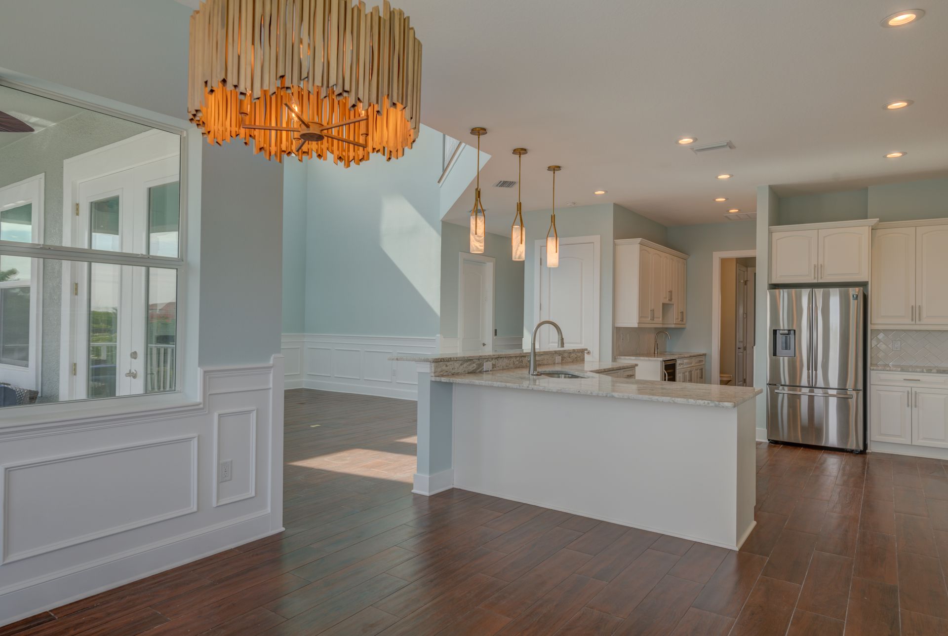 Open-concept kitchen and dining area with white cabinets, stainless steel refrigerator, and wooden floors.
