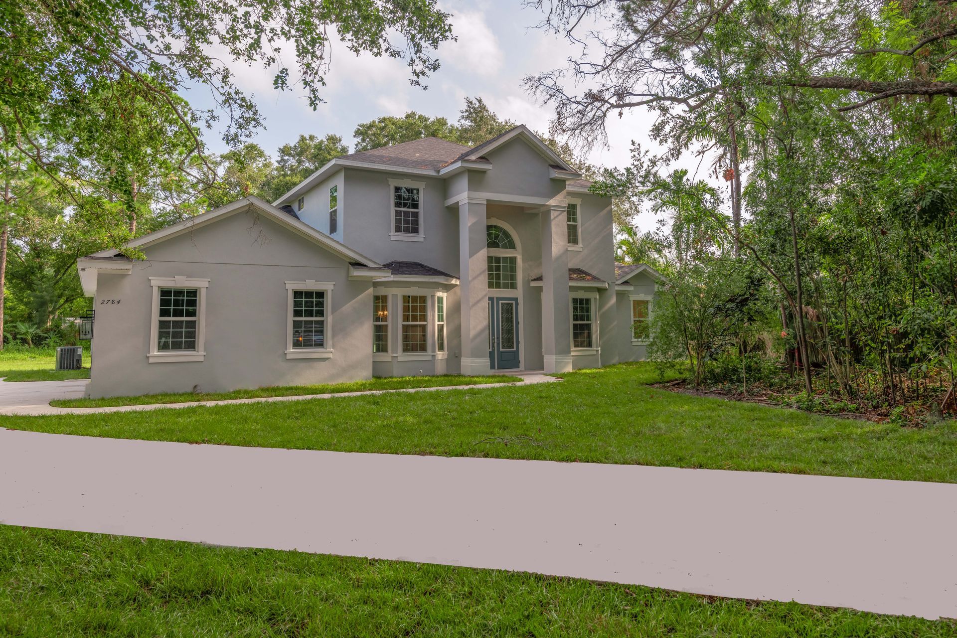 Gray two-story house with green lawn, trees, and blue sky.