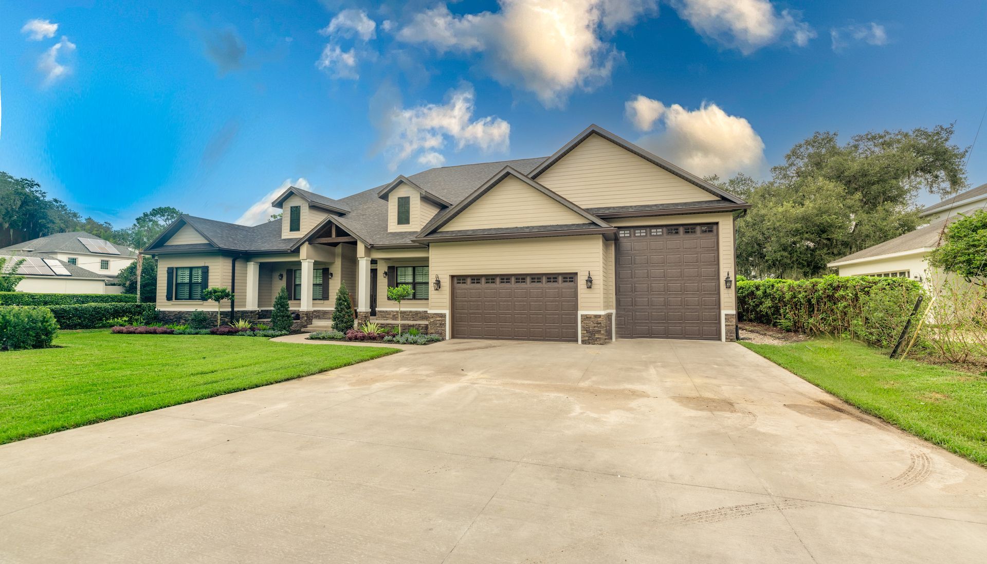 Large beige and brown house with a two-car garage, driveway, and green lawn under a blue sky.