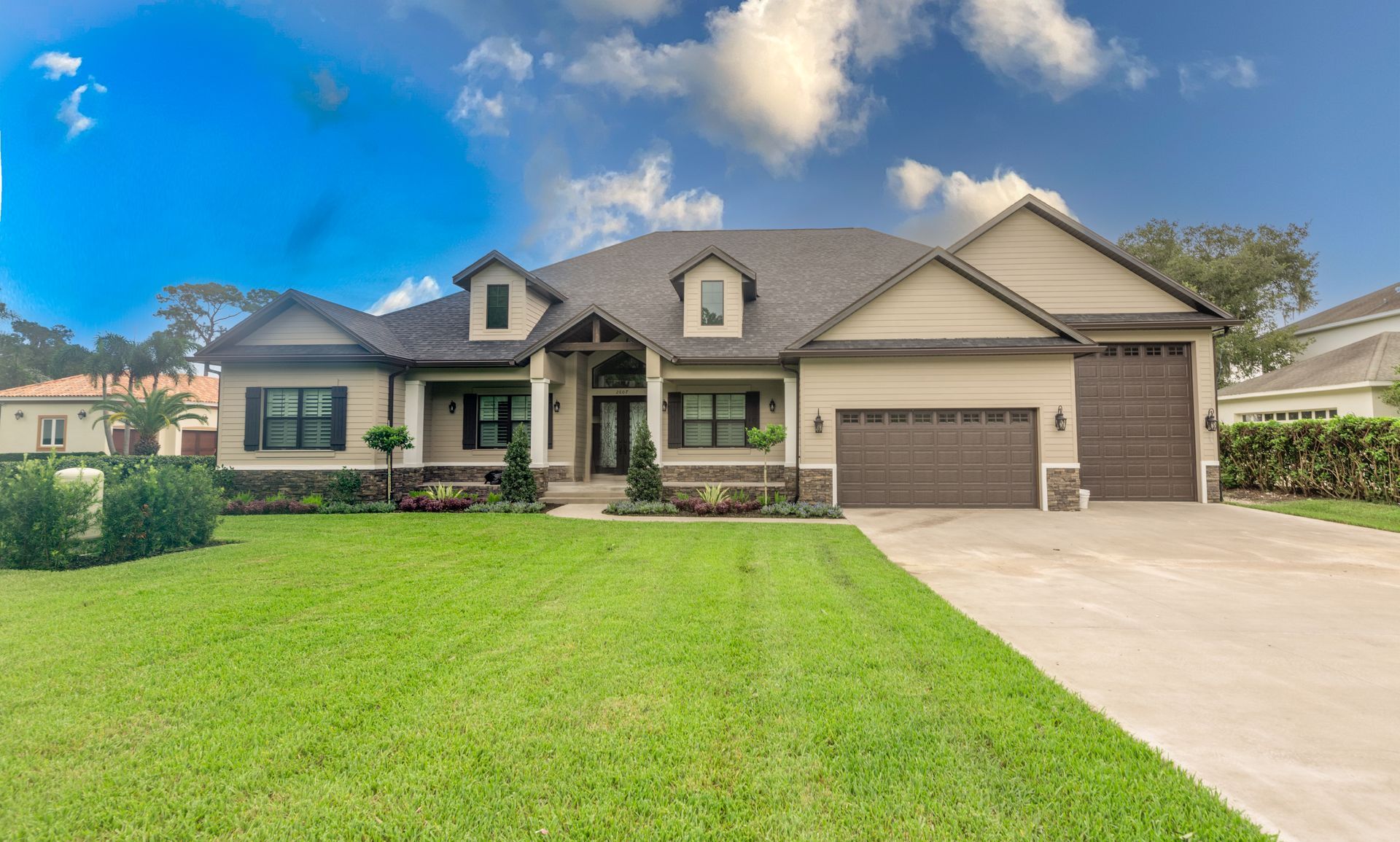 Beige and brown house with a green lawn, two-car garage, and blue sky.