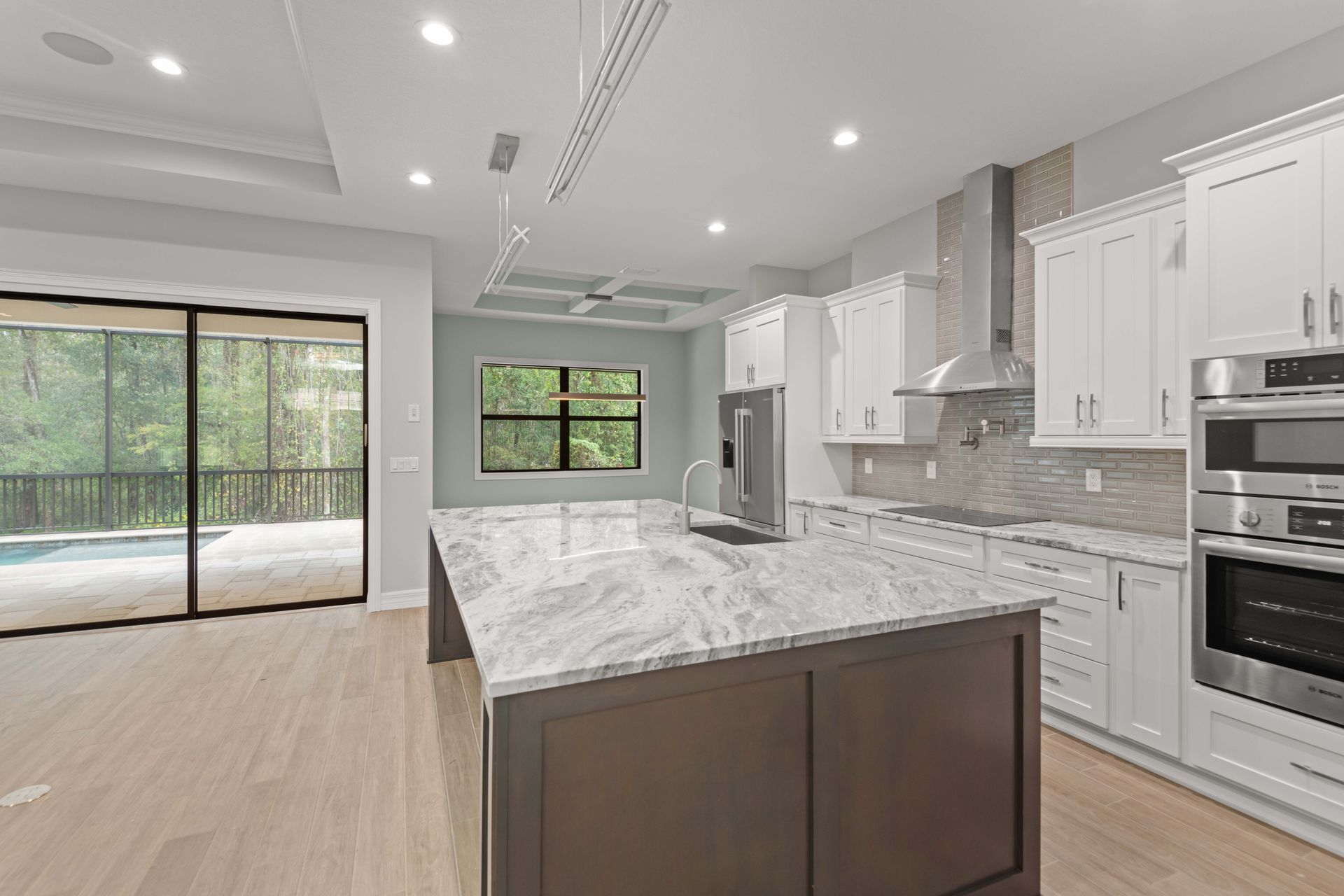 Modern kitchen with large island, white cabinets, stainless steel appliances, and view of a pool.