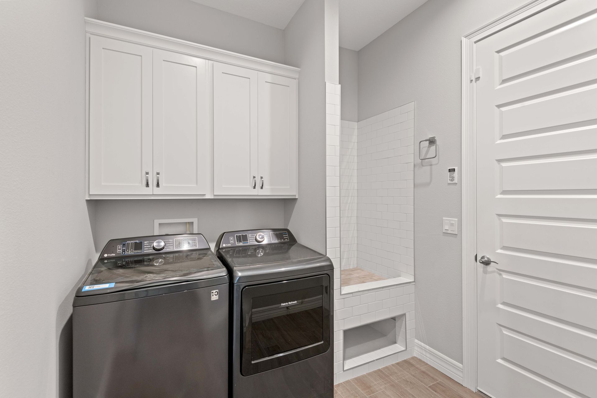 Laundry room with washer, dryer, upper cabinets, a tiled bench, and a closed door.