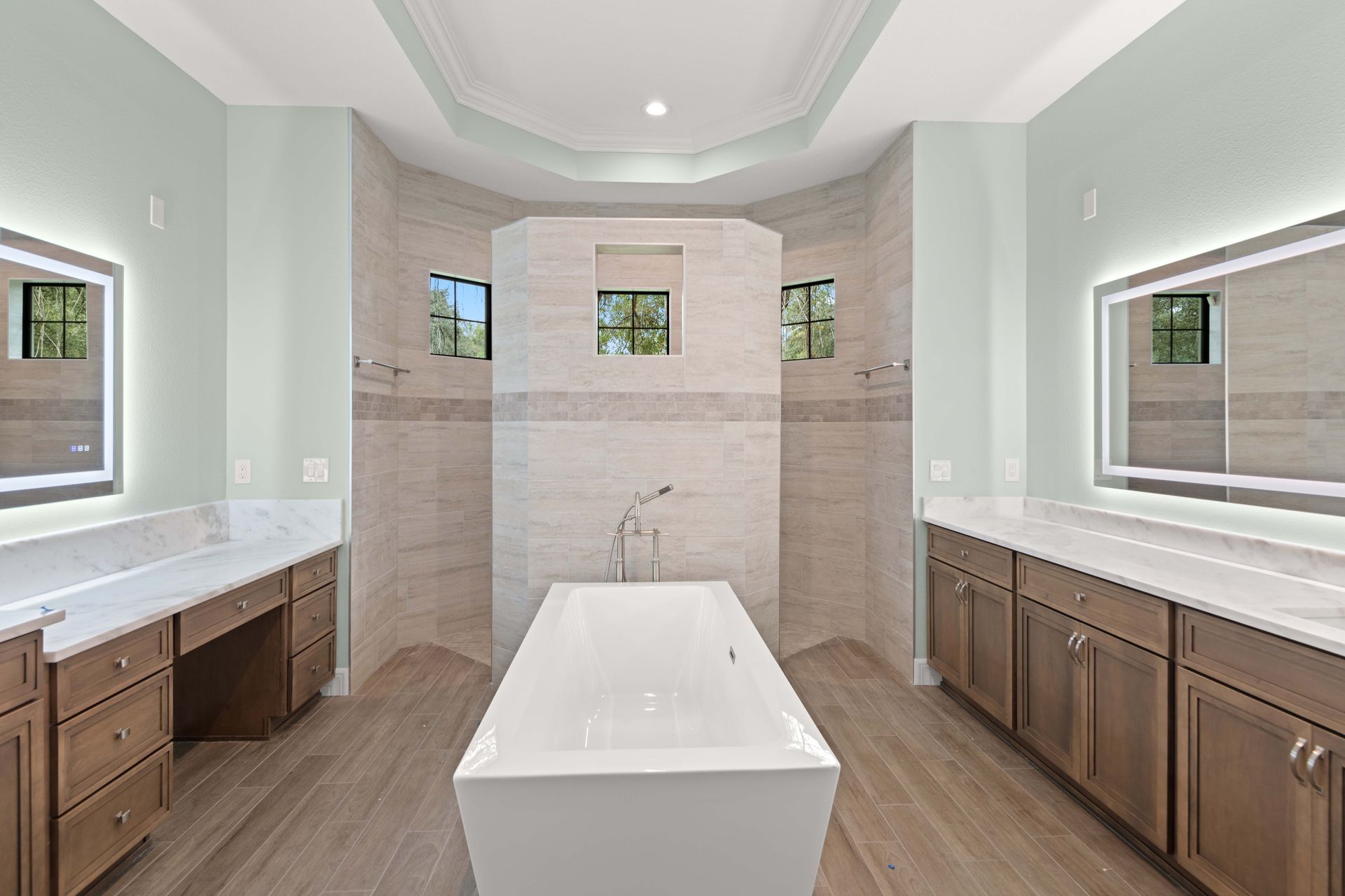Spacious bathroom with a freestanding tub, large mirrors, and two vanities; neutral color palette.